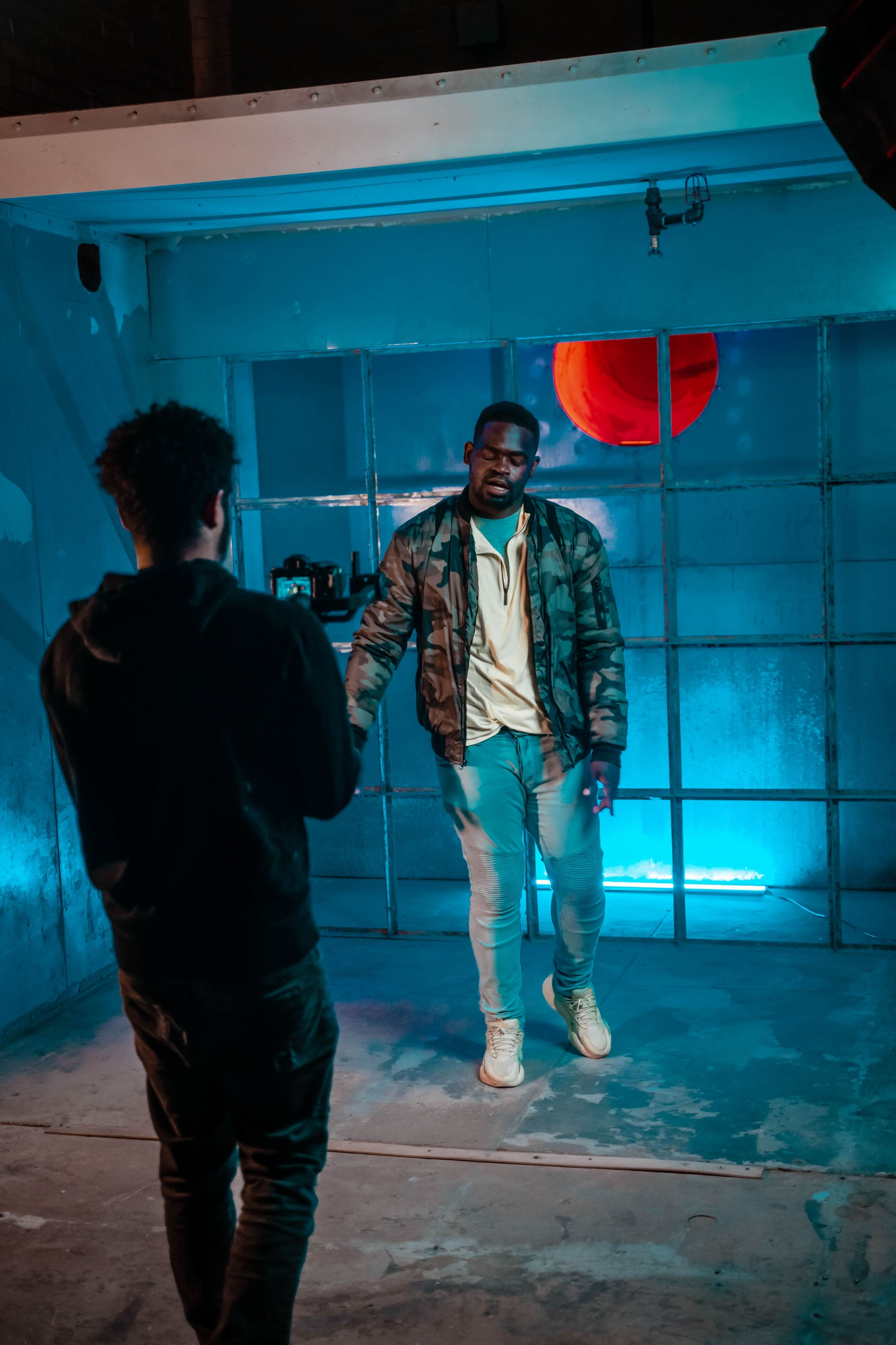 A man poses for a photo against a blue background, while another person holds a camera and captures the moment.