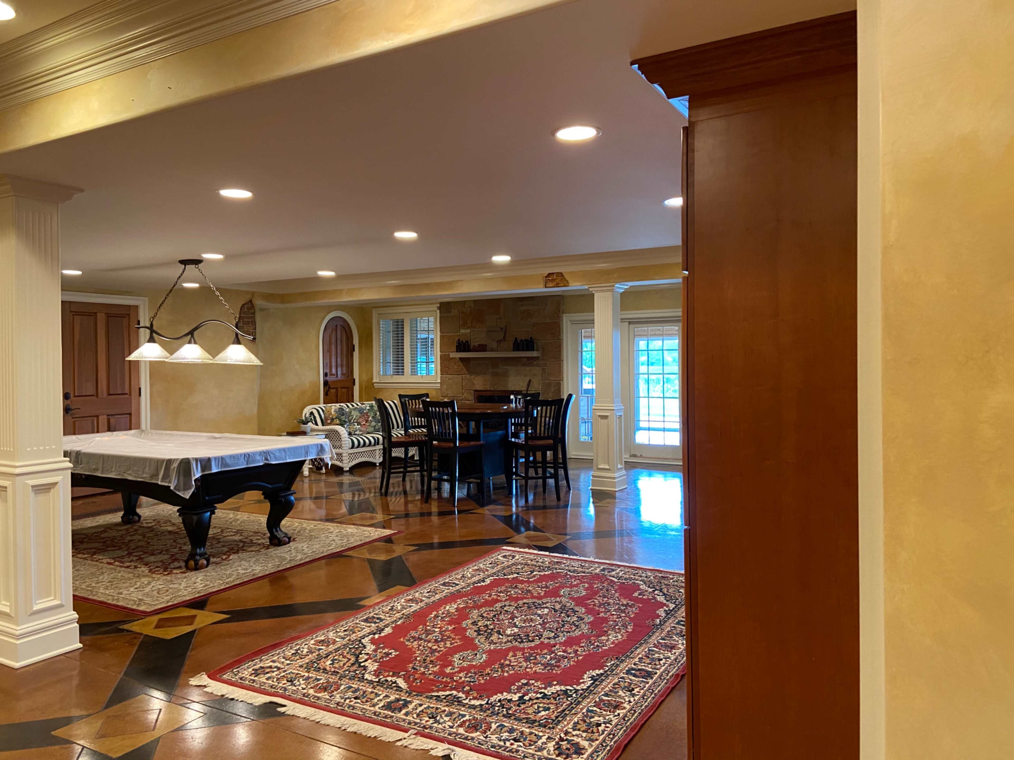 A spacious interior room with a pool table, dining area, and patterned rugs.