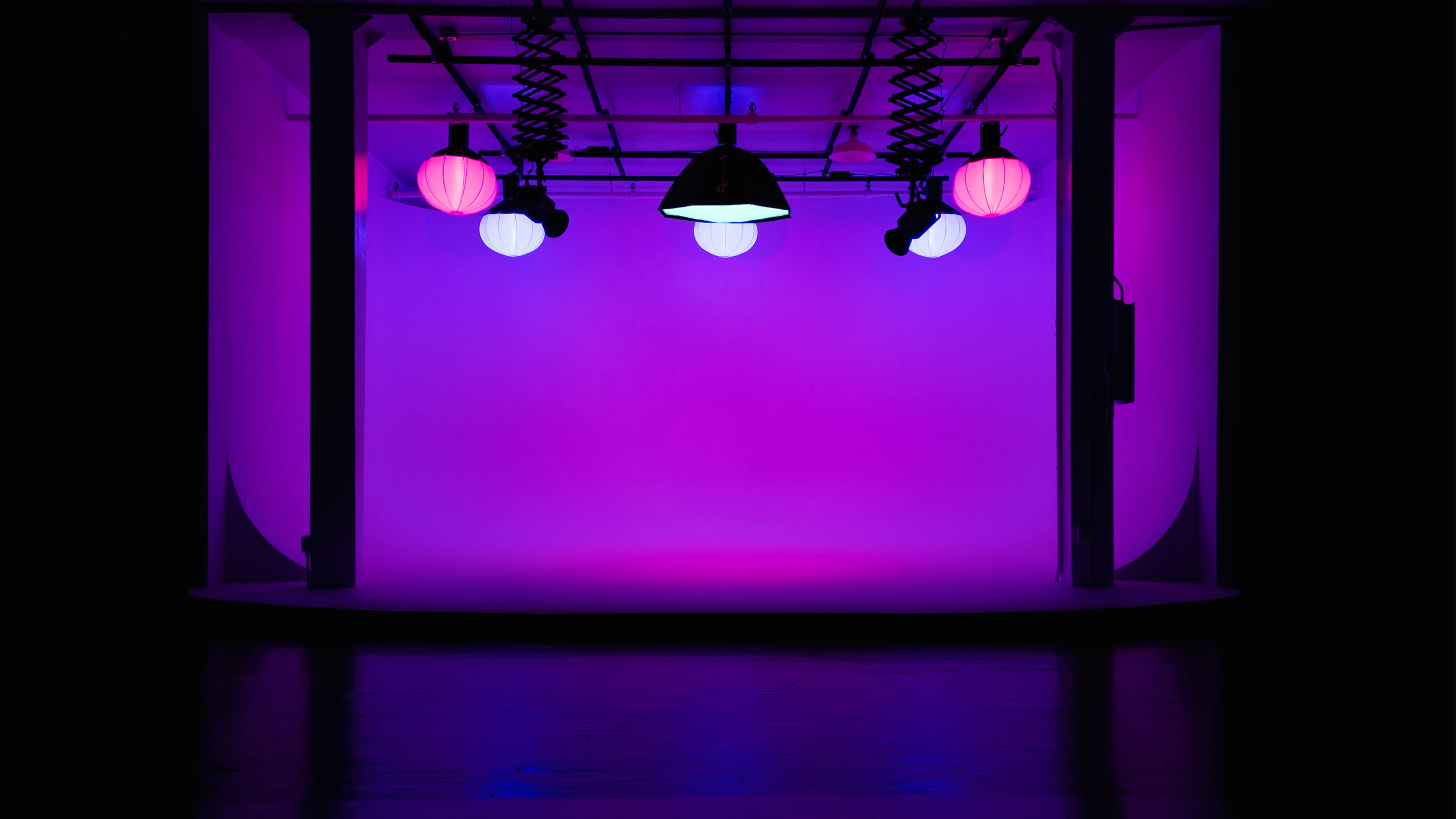 The image shows a minimalist studio space with a gradient purple background lit by various hanging lamps.
