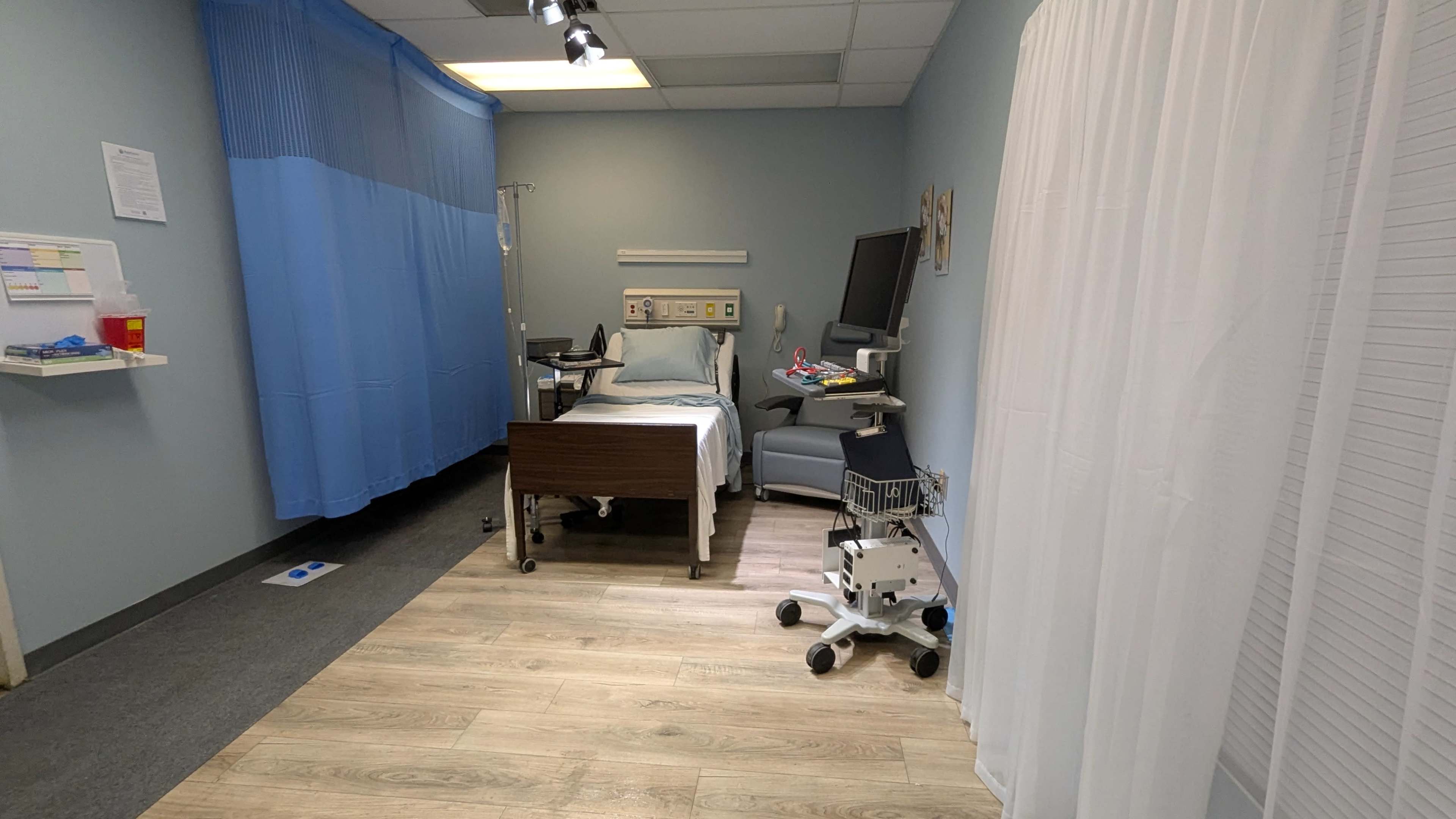 The image shows a hospital room with a bed, medical equipment, and a curtain dividing the space.