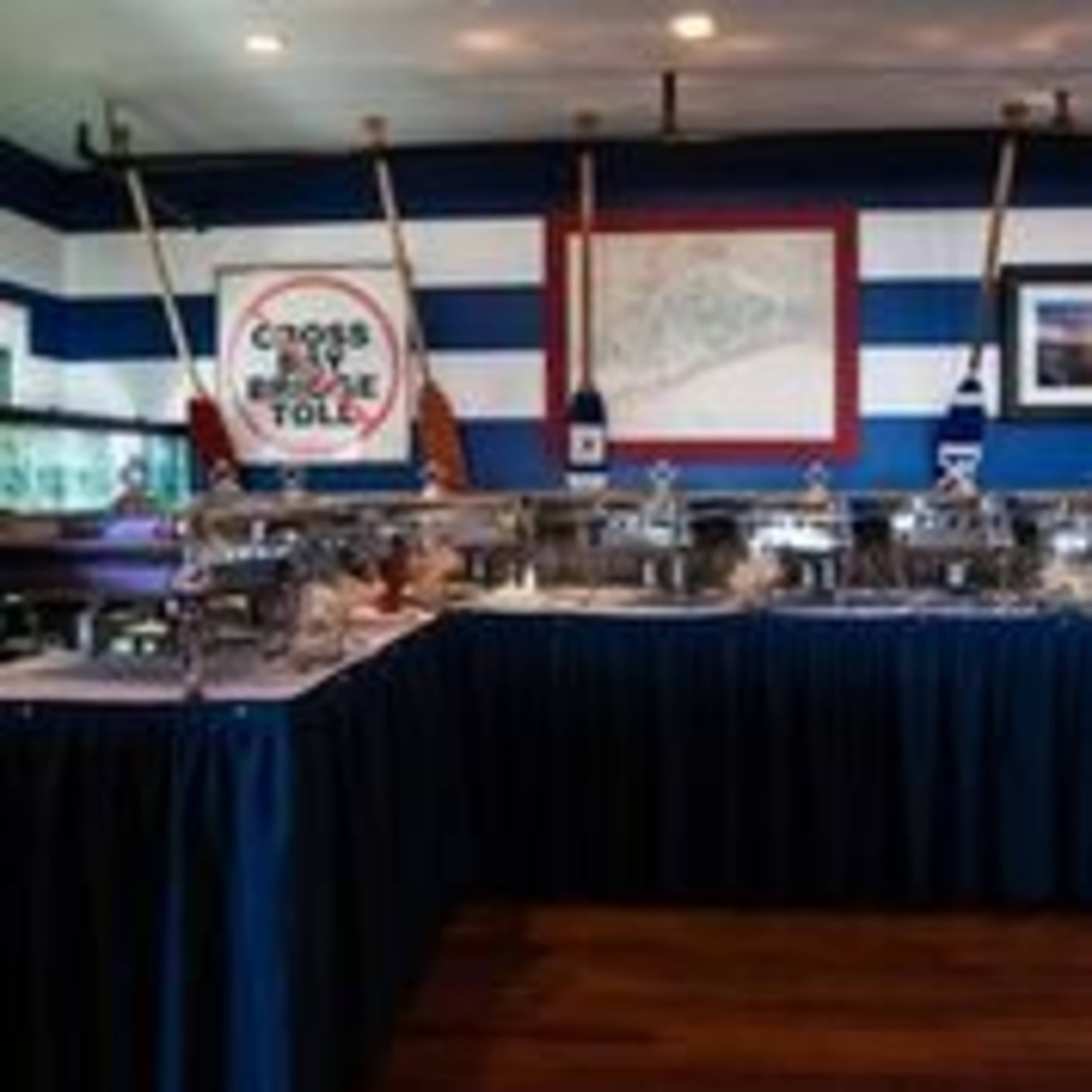 A buffet setup with rows of chafing dishes arranged on tables with dark blue tablecloths, against a striped blue and white wall.