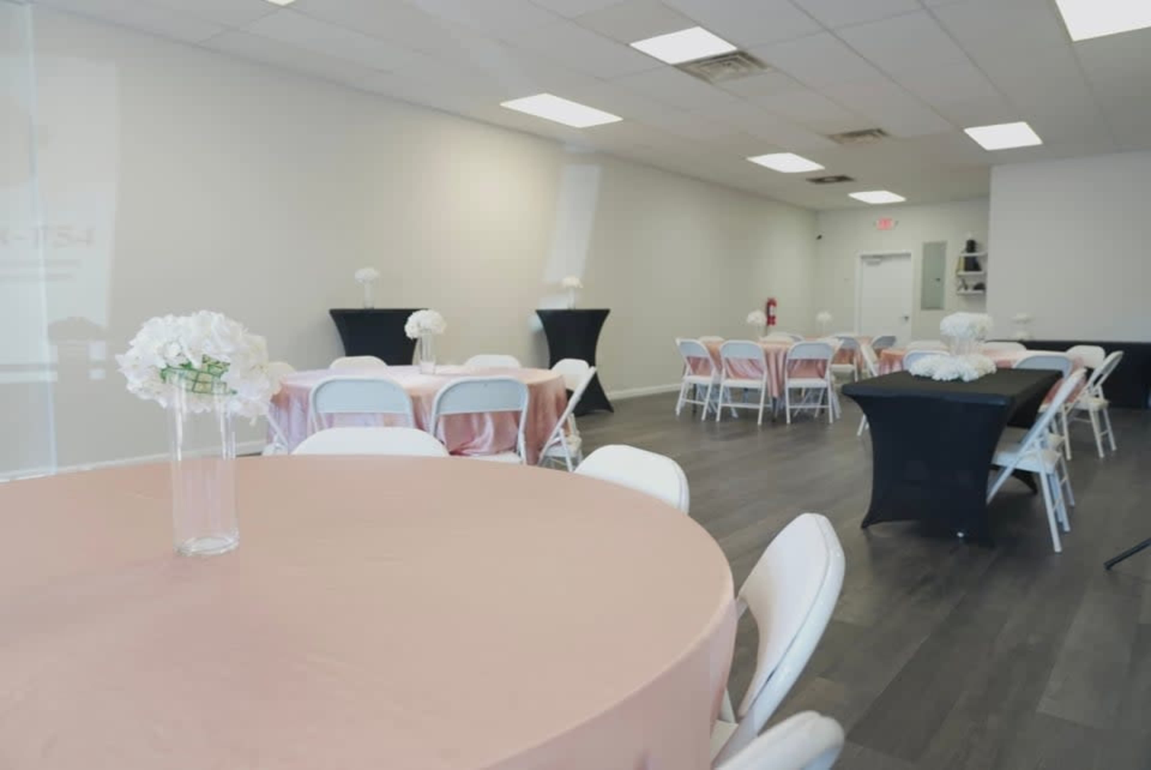 The image shows a well-lit event space with several tables covered in pink and black table linens, arranged for a gathering.