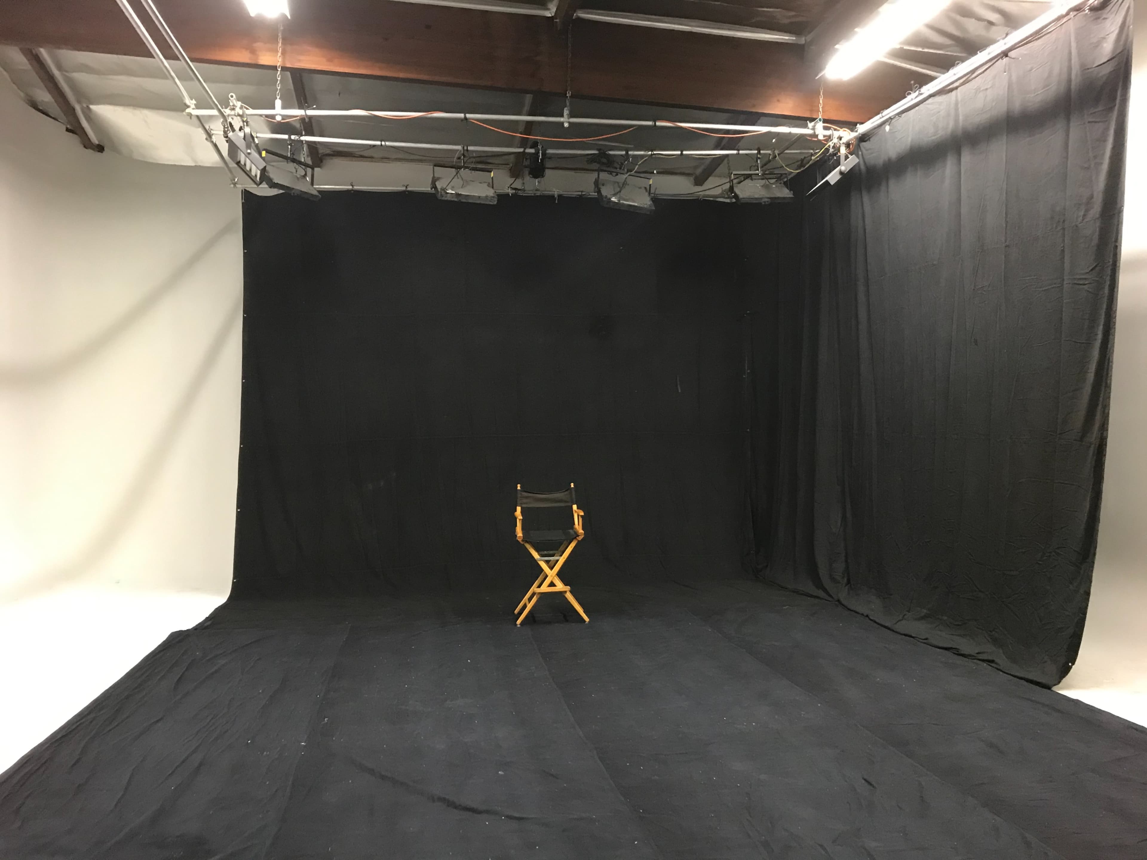 A dimly lit photography studio with a black backdrop and a single wooden director's chair placed in the center.