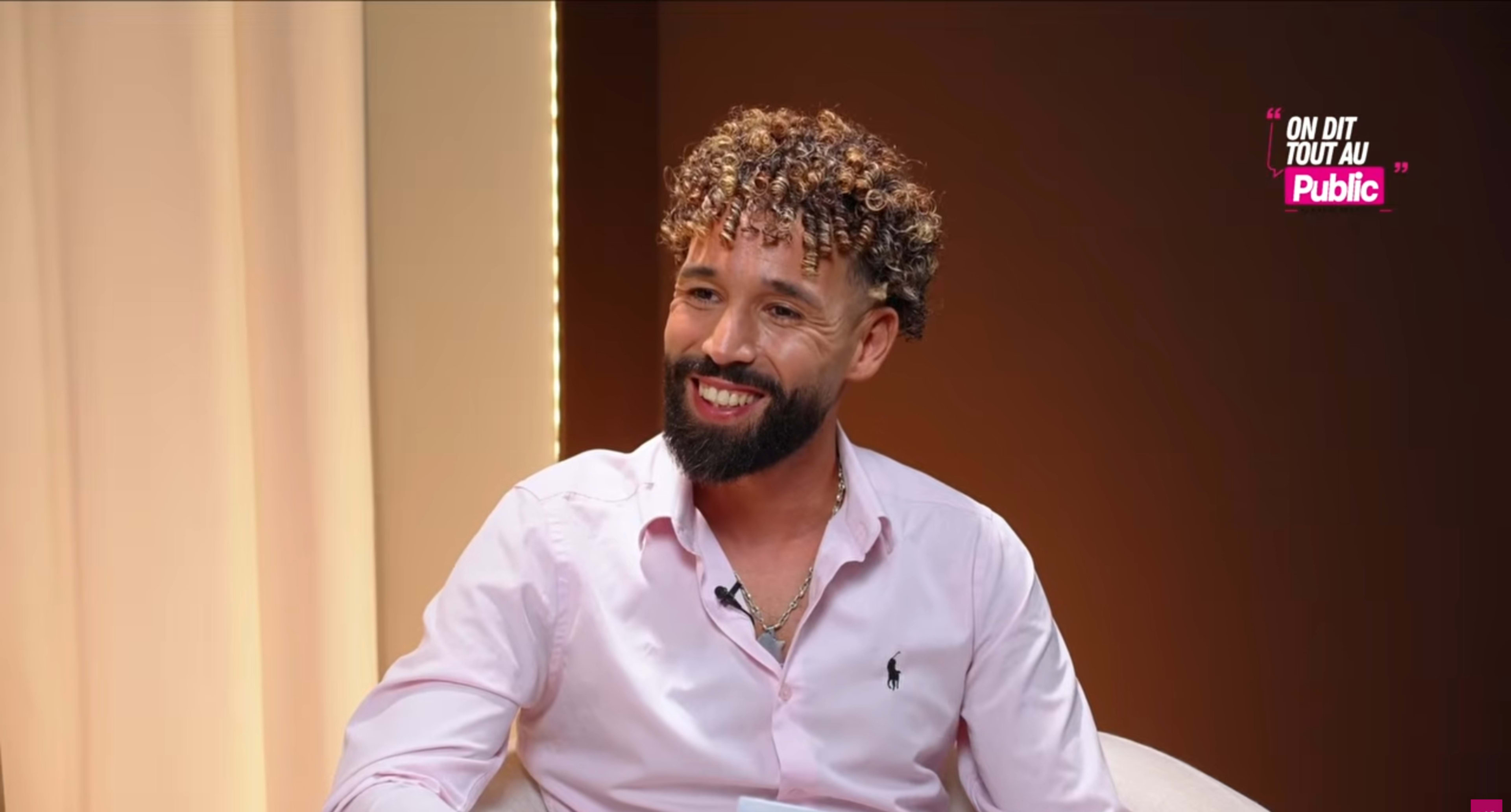 A man with curly hair is seated and smiling during an interview.