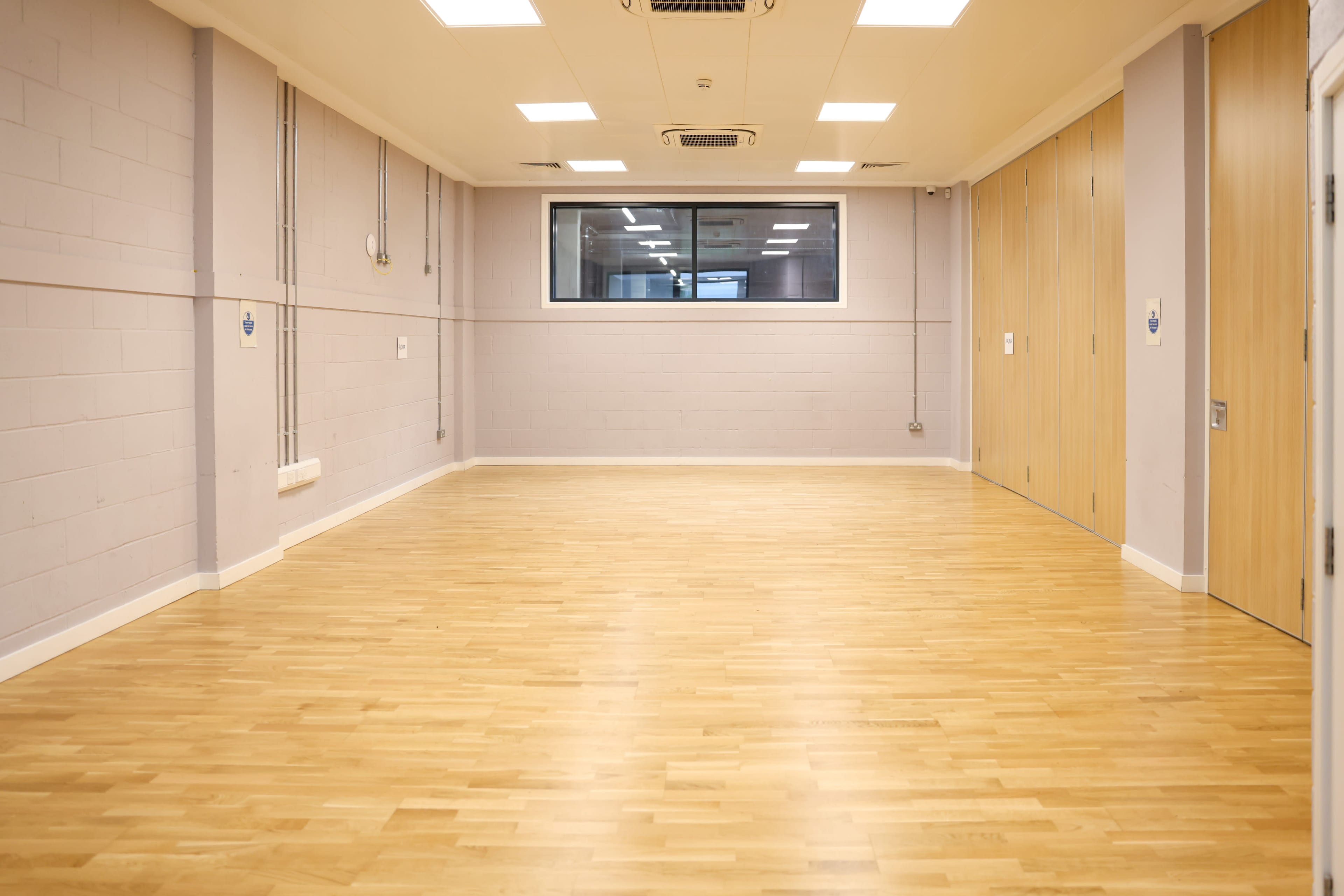 An empty room with light wooden flooring, gray walls, and a window on one side.