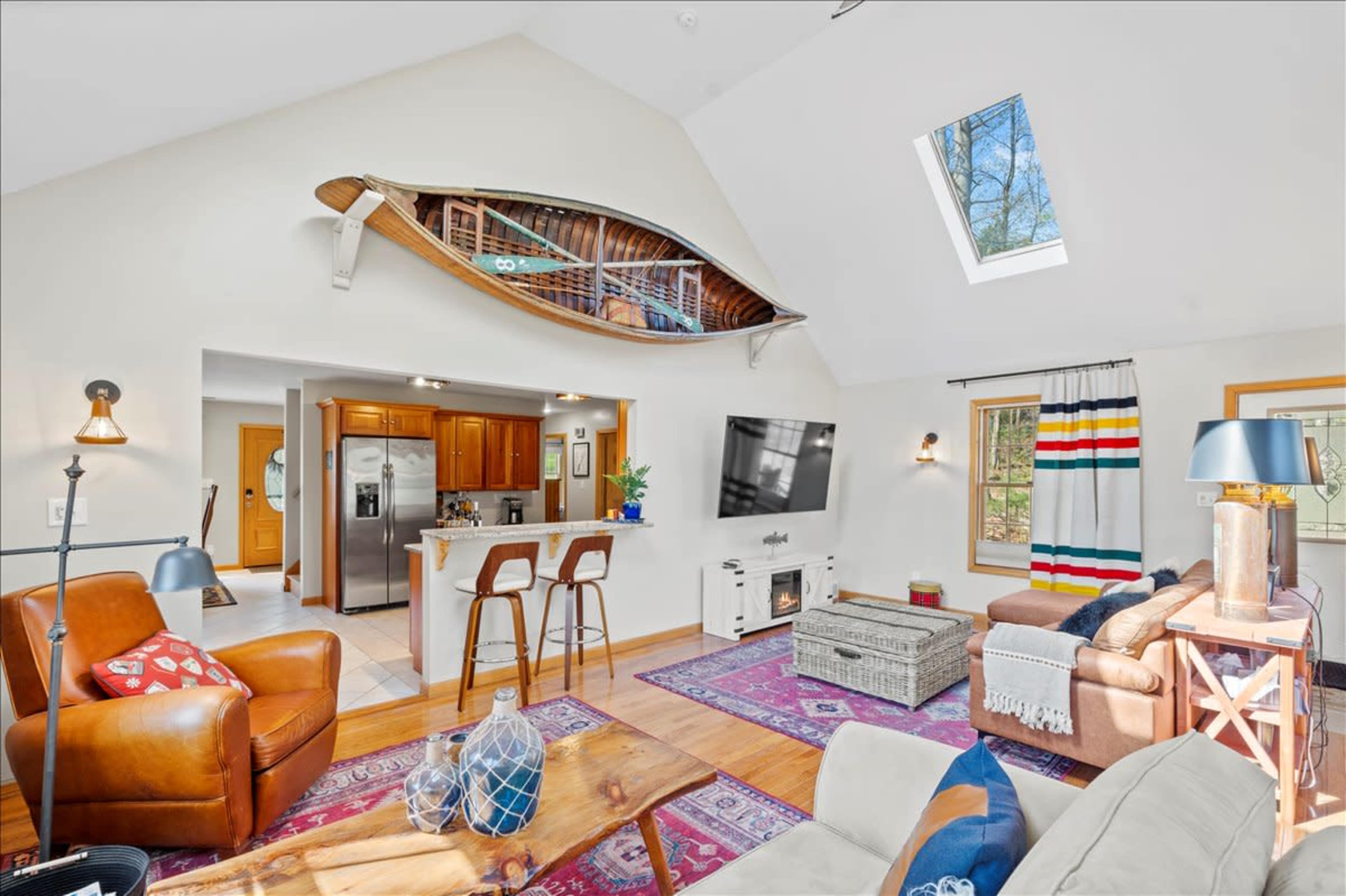 The living space features a high ceiling, a wooden canoe mounted on the wall, a cozy seating area, and a kitchen with modern appliances.