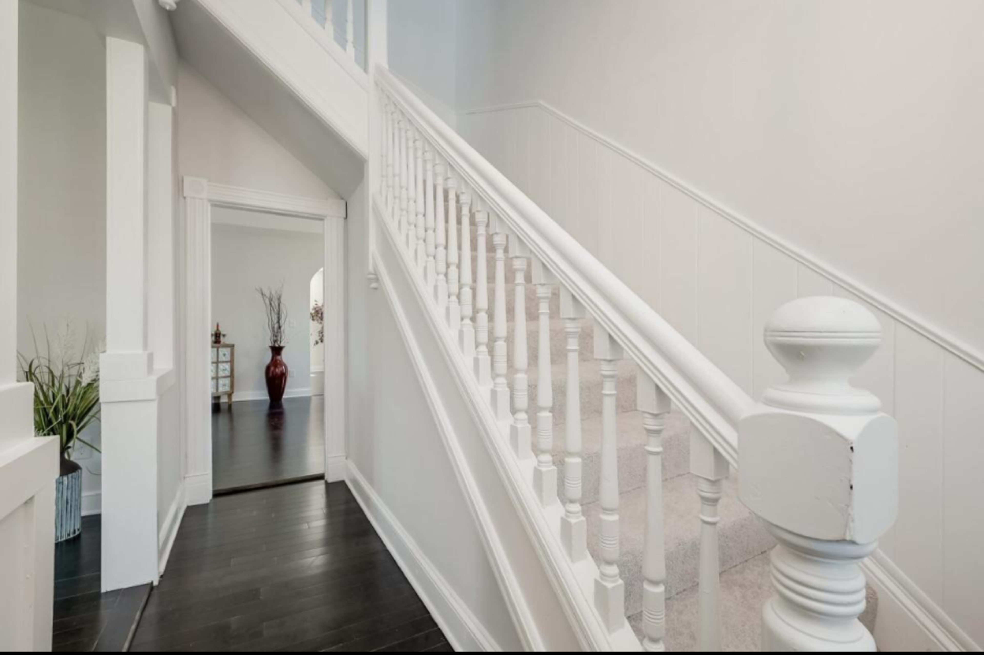 A staircase with white wooden balustrades ascends alongside a light-colored hallway in a well-lit home.