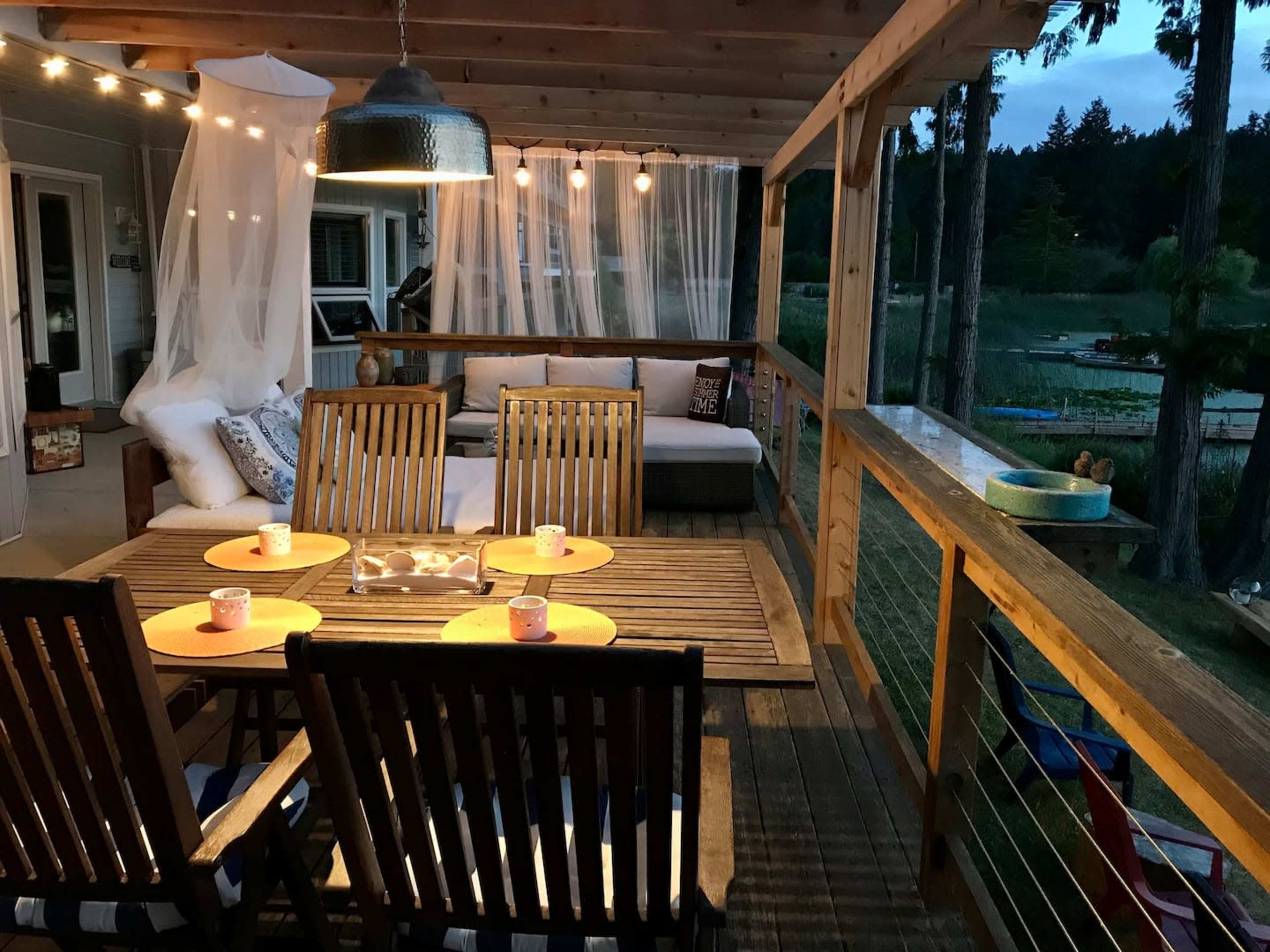 A wooden deck area with a table set for dining, surrounded by string lights and a cozy seating arrangement.