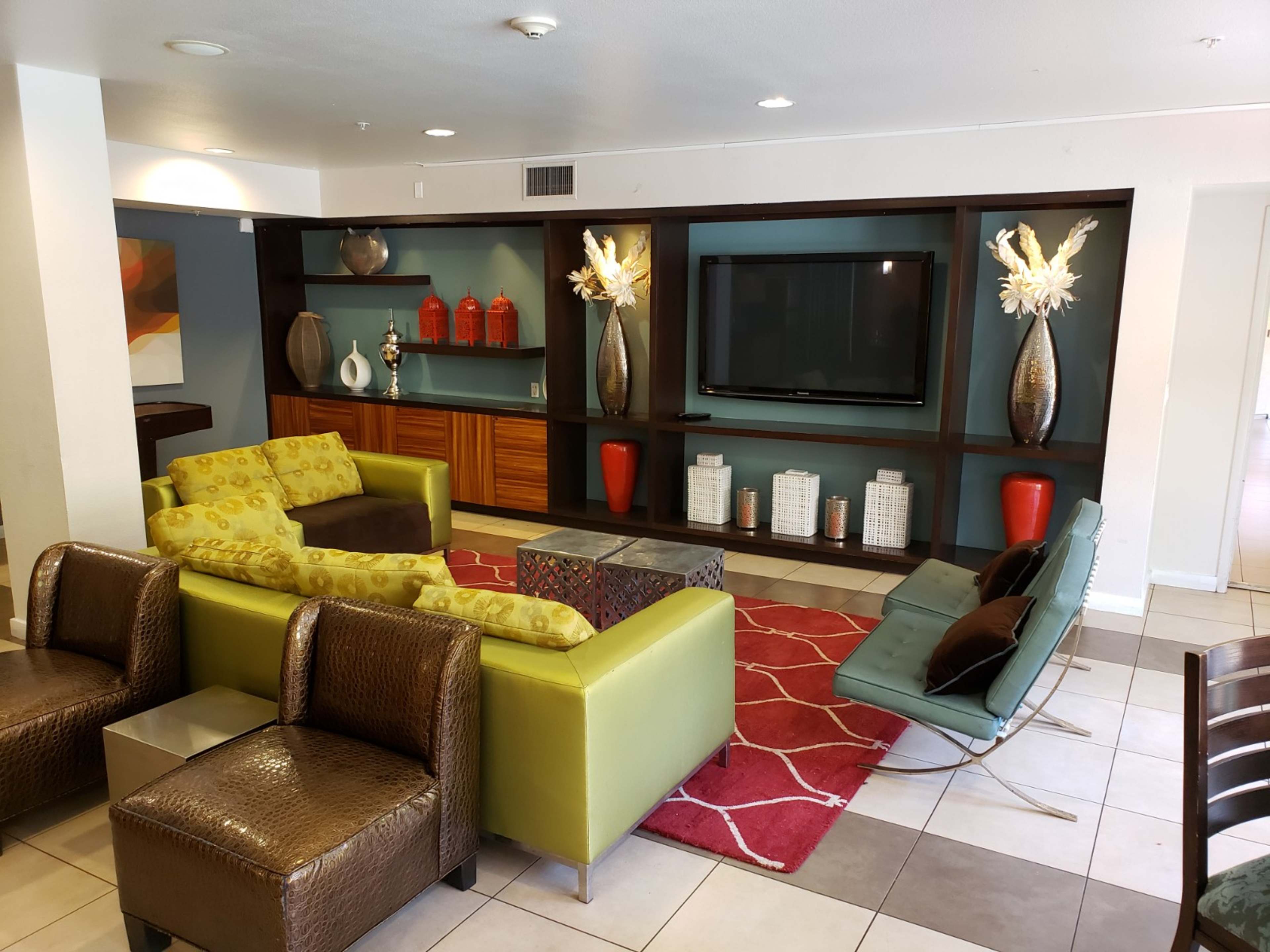 A seating area featuring a green couch, brown leather chairs, and colorful decor, centered around a television and a patterned rug.