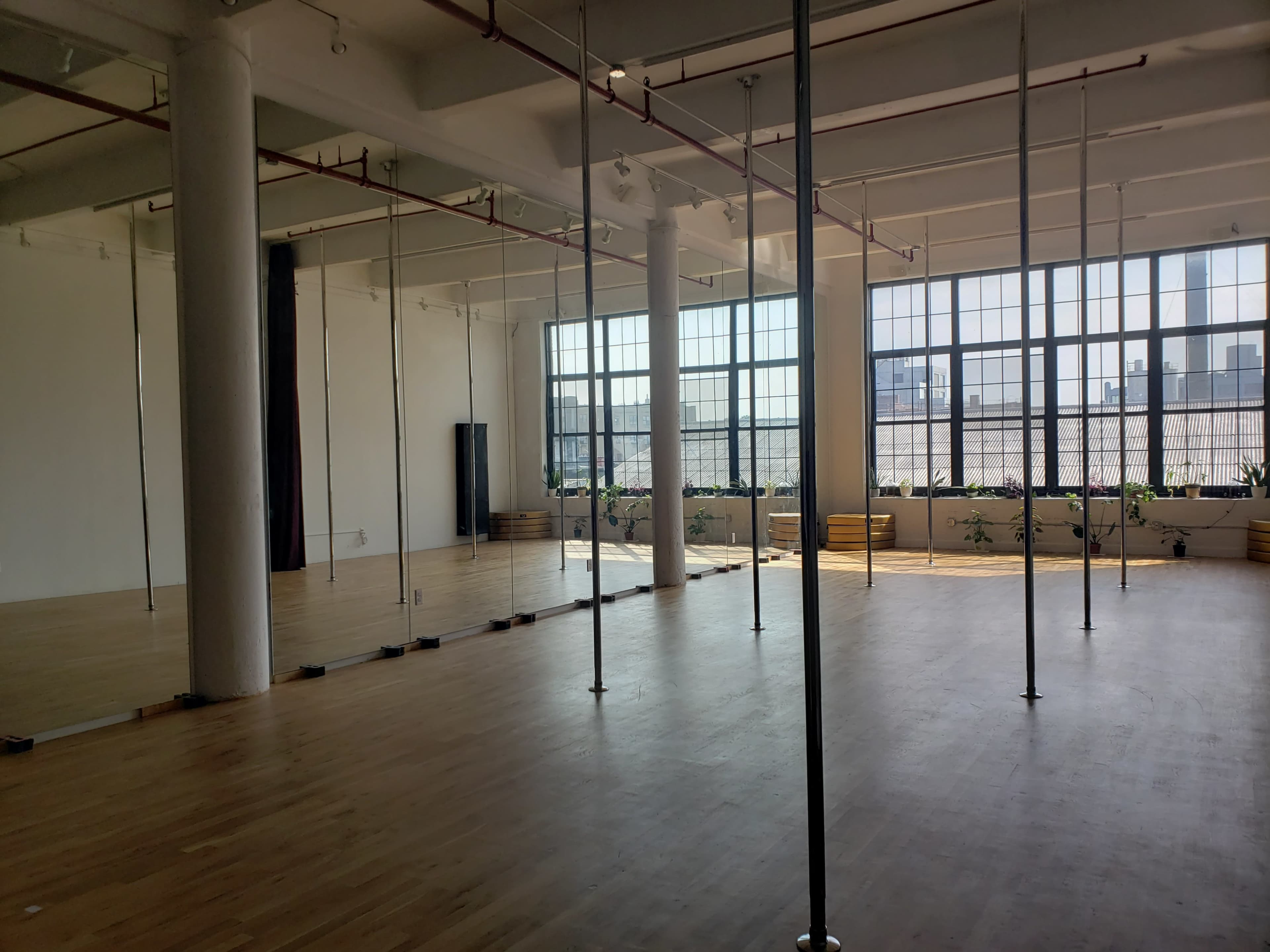 A spacious dance studio with wooden floors, large windows, and multiple mirrors along the walls.