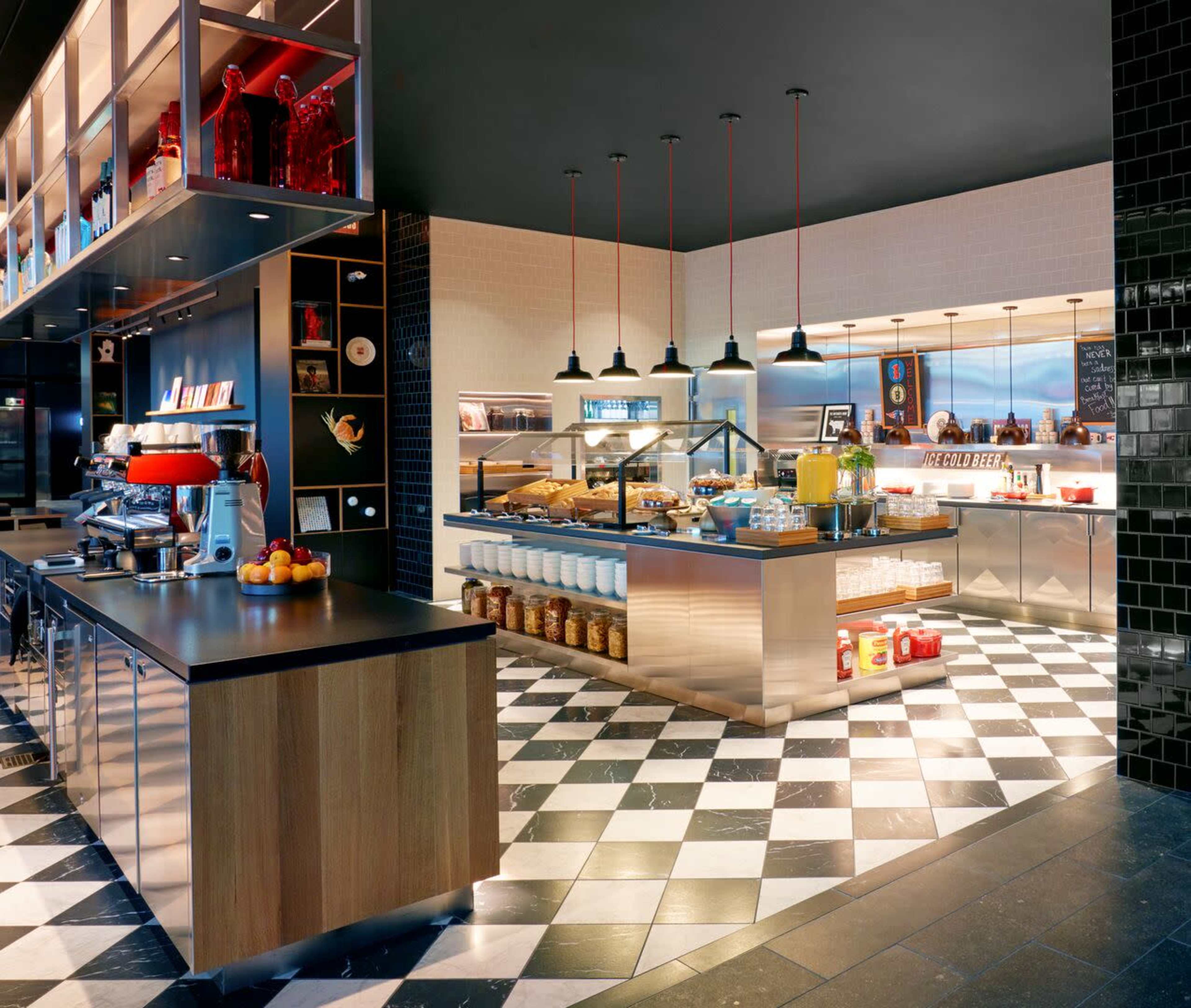 The image shows a modern café interior with a checkerboard floor, display shelves, and a counter featuring a variety of food and beverages.