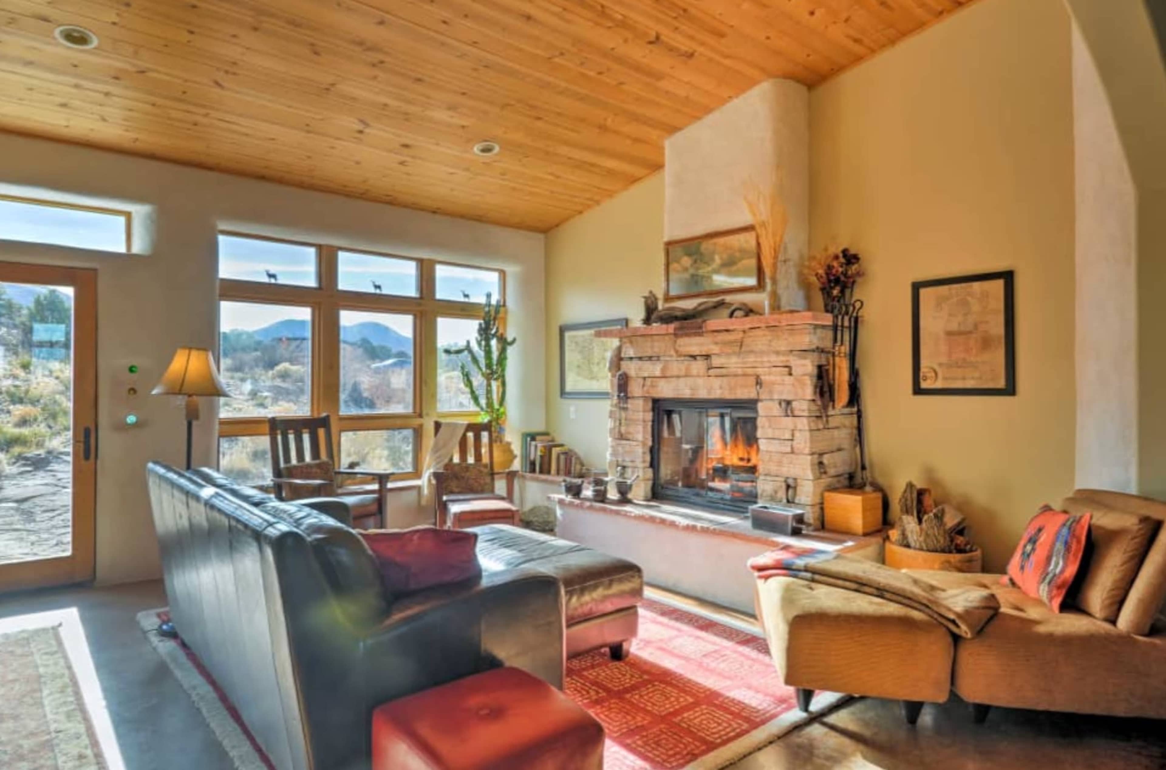 The room features a stone fireplace as the centerpiece, surrounded by seating and large windows that overlook a desert landscape.