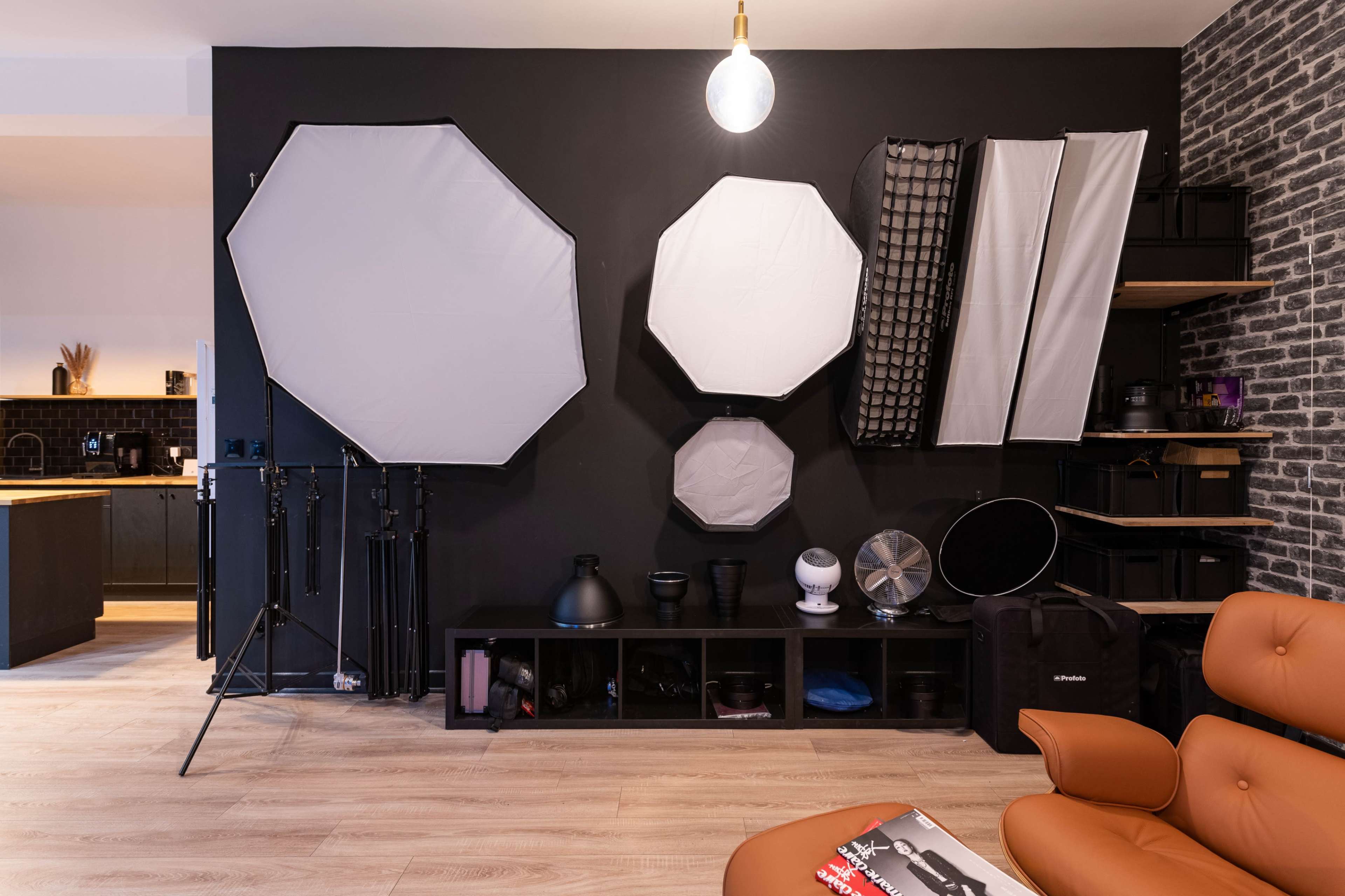 The image shows a studio space with various photography light modifiers, including softboxes and a reflector, mounted on a black wall alongside storage units and a fan.