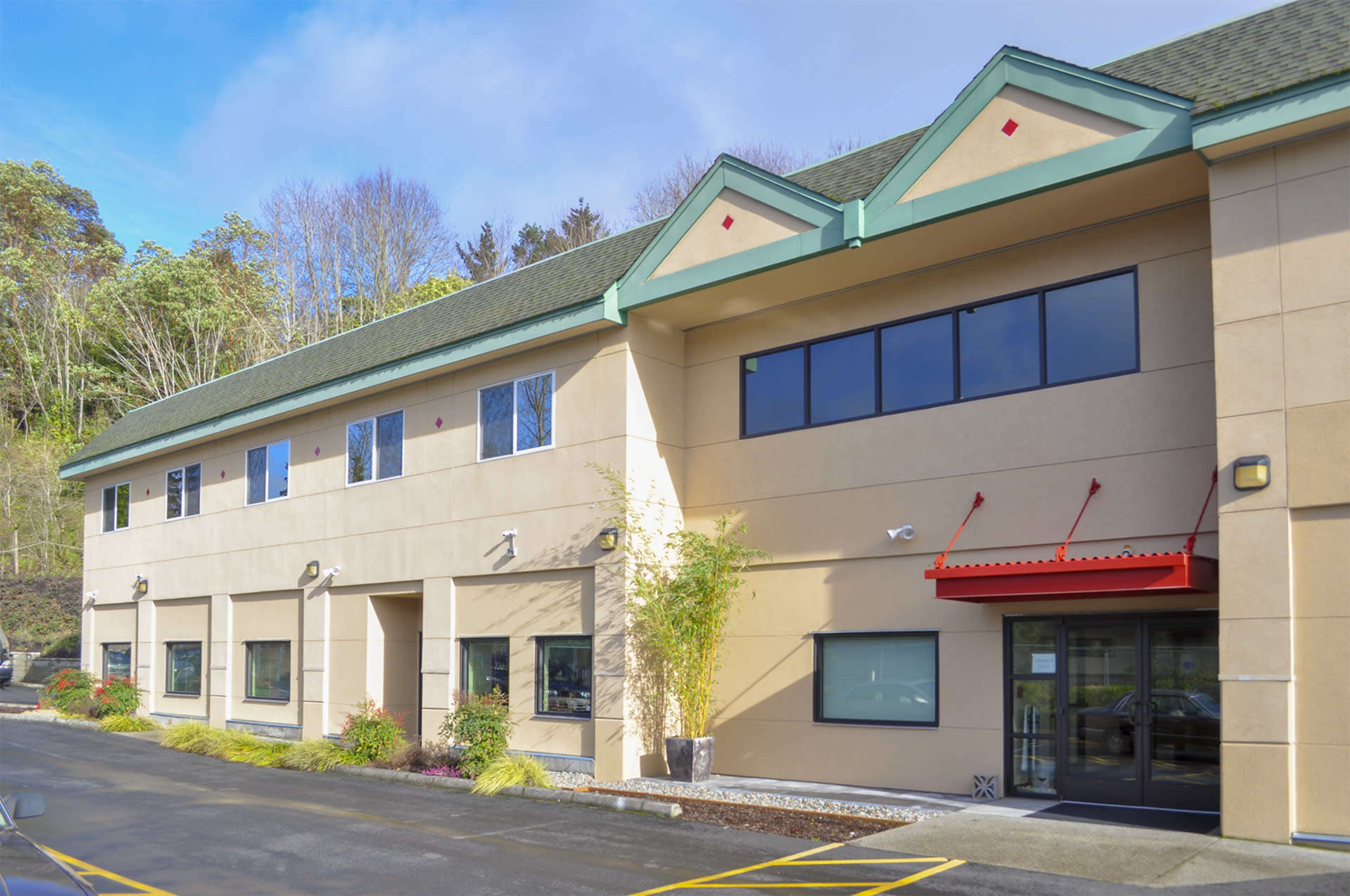 A two-story commercial building with a tan exterior, large windows, and a red canopy over the entrance.