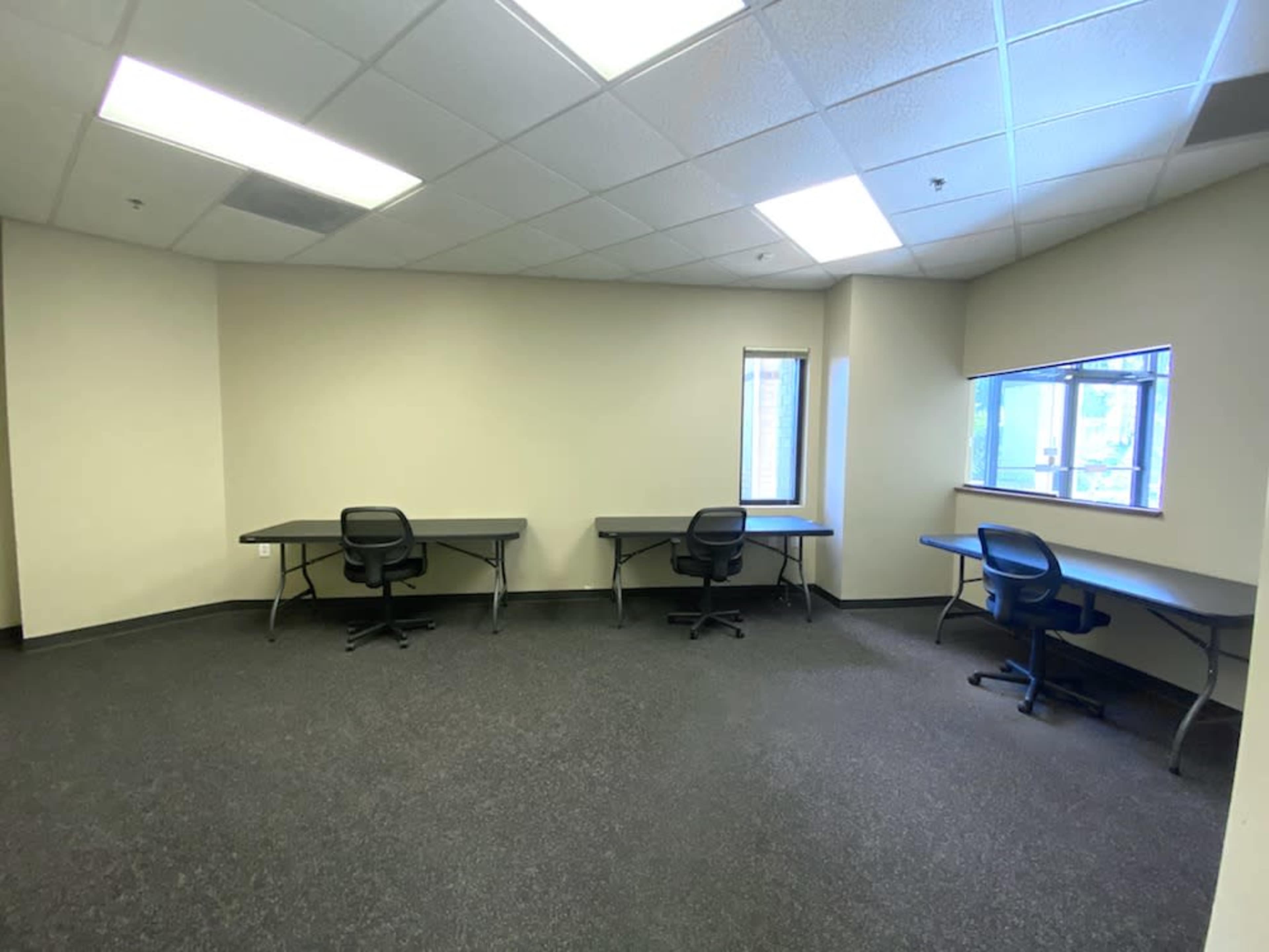A vacant office space with two tables and chairs arranged in a semi-circular layout against the walls.