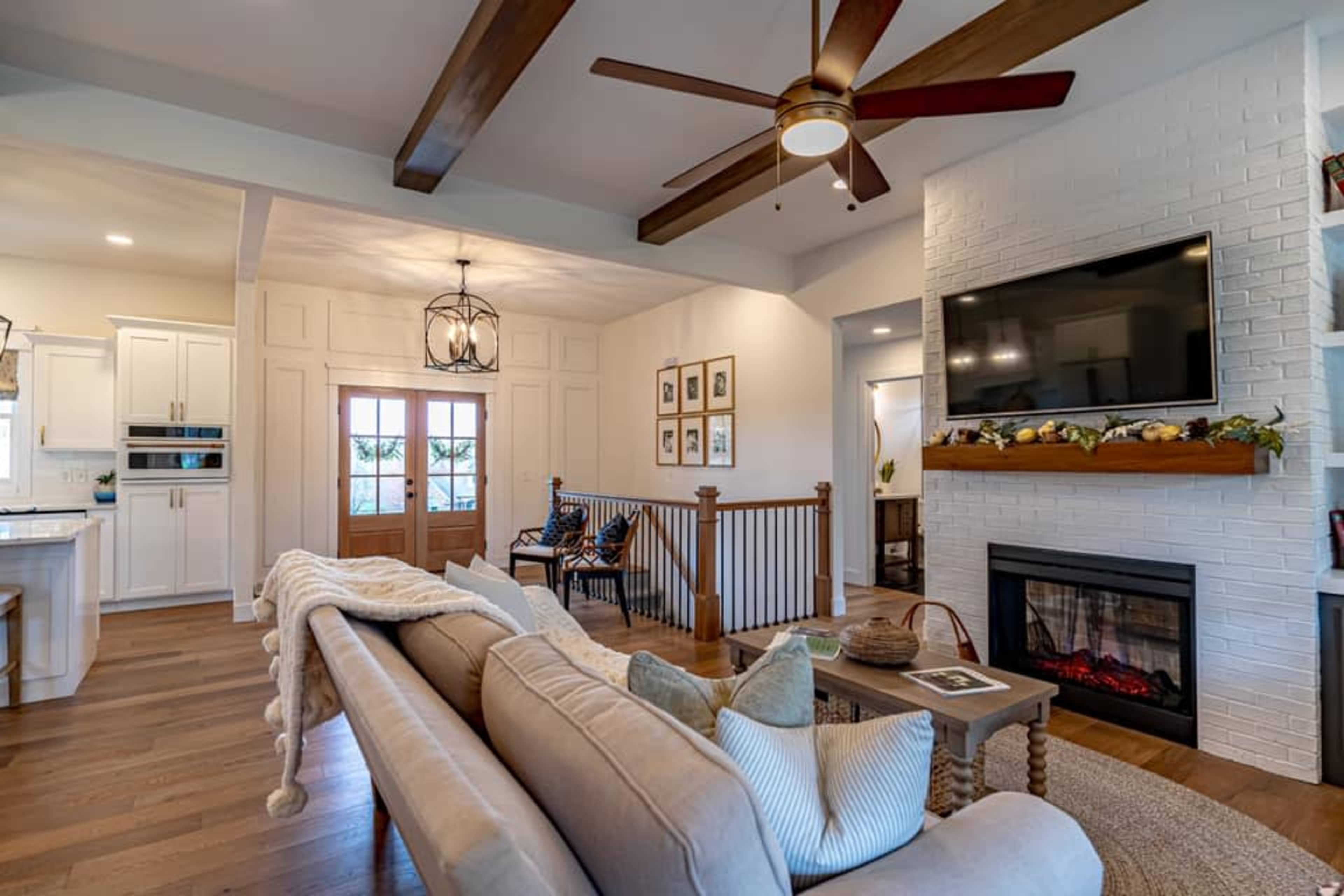 A living room with a sofa, fireplace, and wooden beams on the ceiling, featuring a front entrance with double doors.
