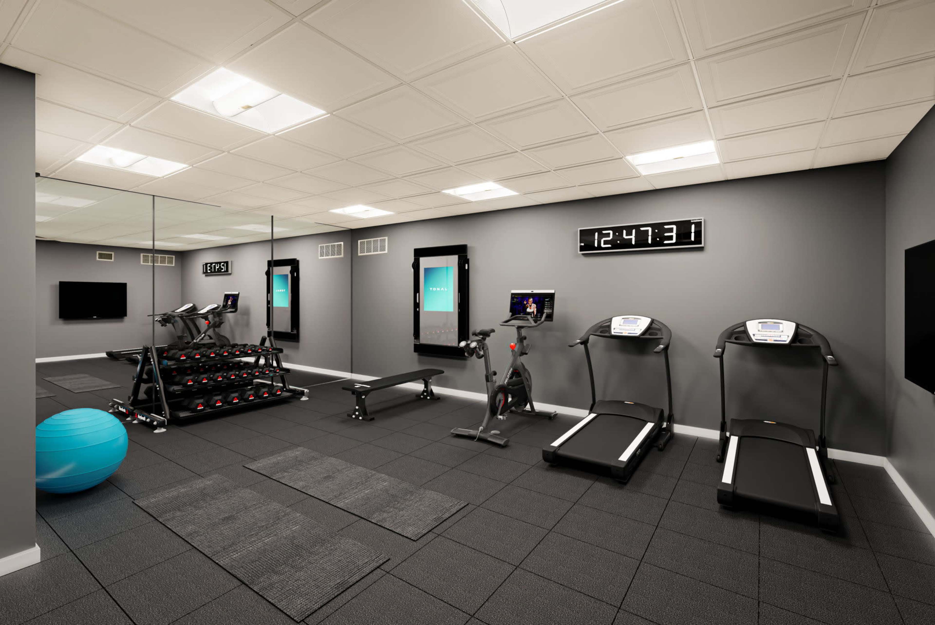 The image shows a modern home gym equipped with treadmills, a stationary bike, weights on a rack, and a large mirror reflecting the space.