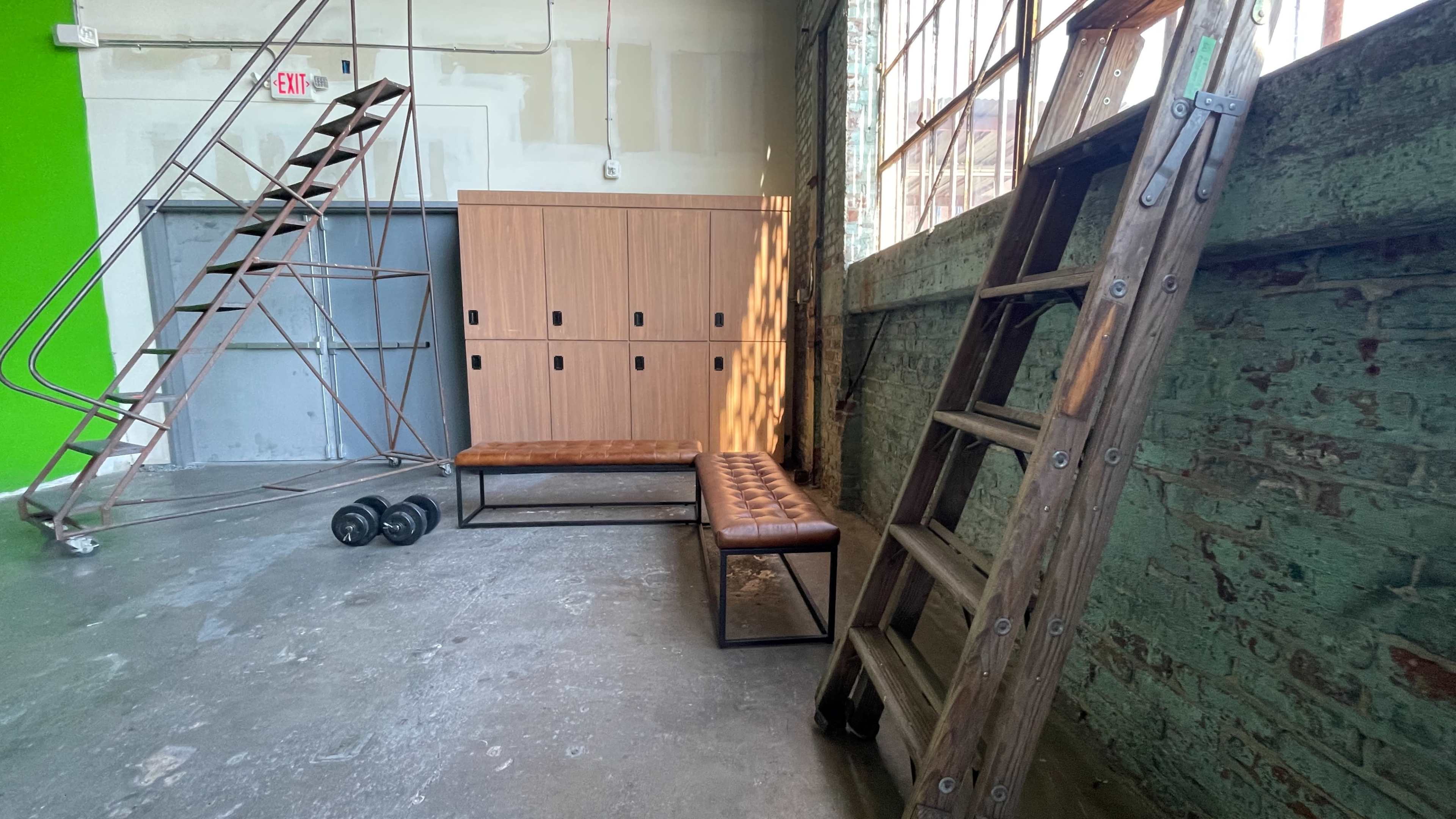 A spacious industrial room with wooden benches, a ladder, dumbbells, and a green wall.
