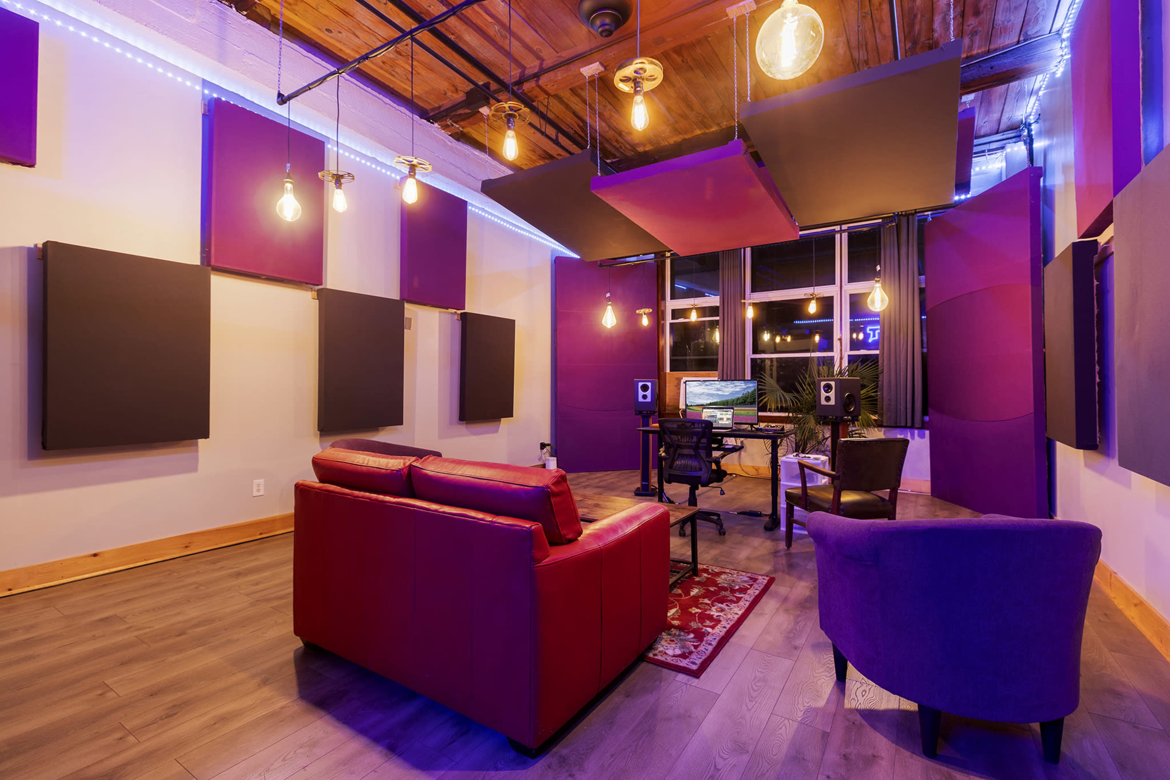 A recording studio with acoustic panels on the walls, a desk with equipment, and seating areas arranged around the space.