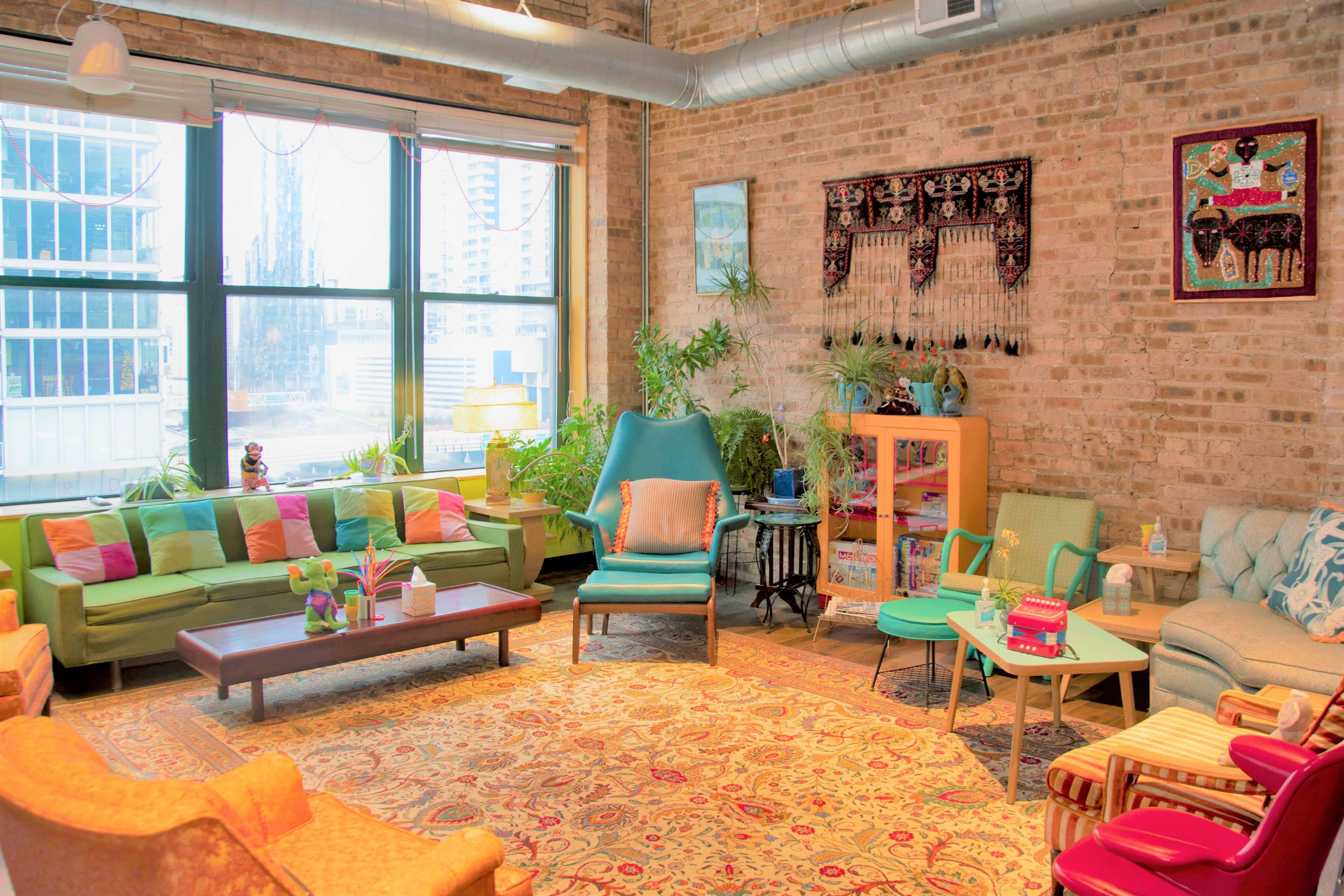 A cozy living room with colorful furniture, plants, and a large window allowing natural light.