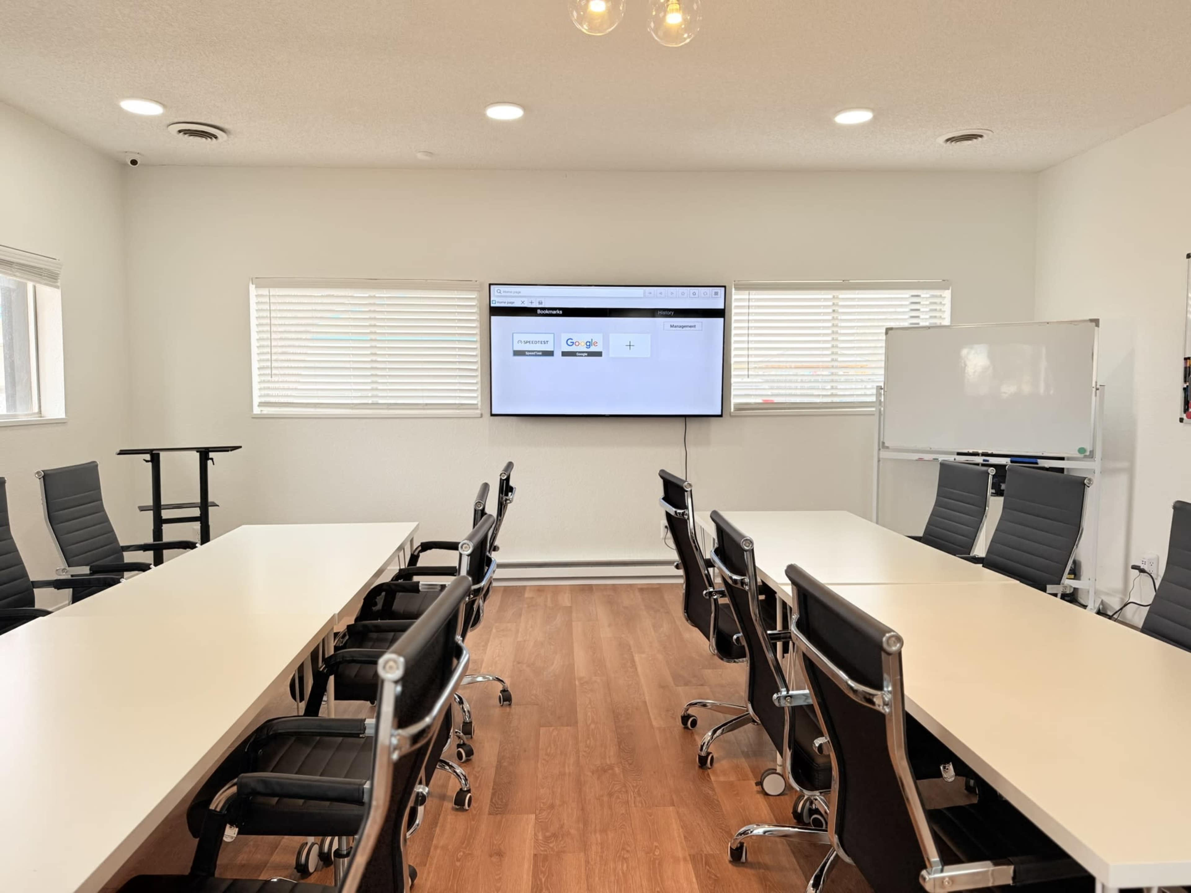 A modern conference room features two long tables with black chairs, a large screen displaying a Google search page, and whiteboards against the walls.