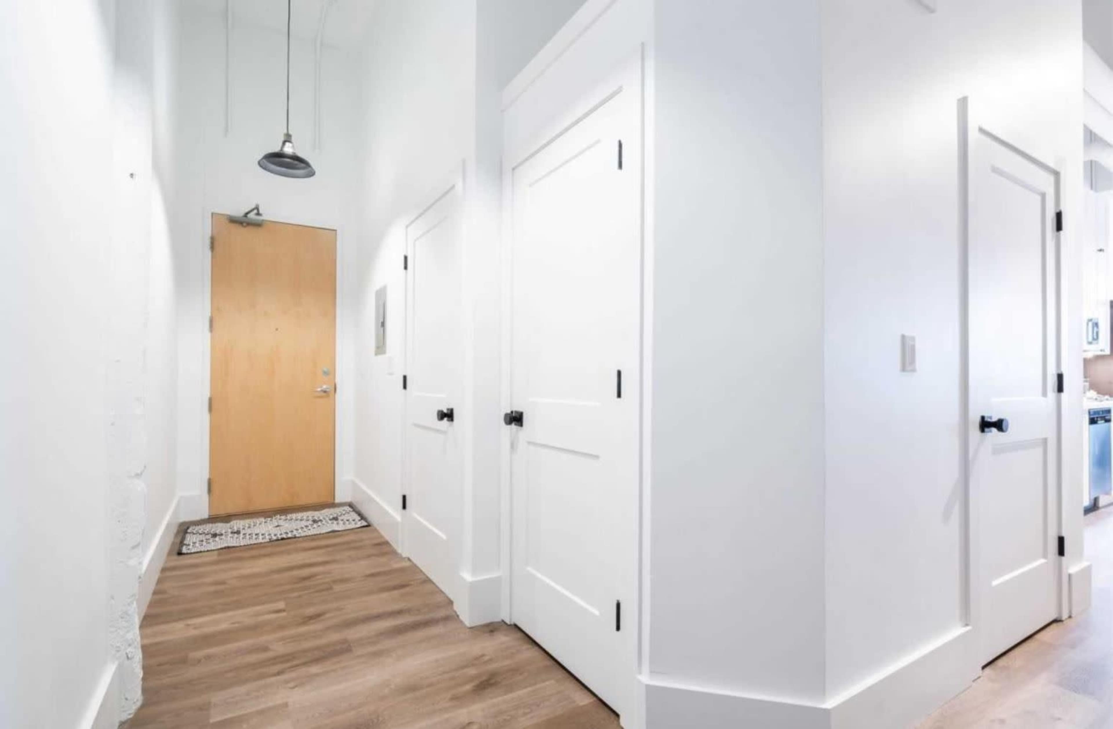 A bright hallway with white walls, a wooden door at the end, and two closed doors on the right.