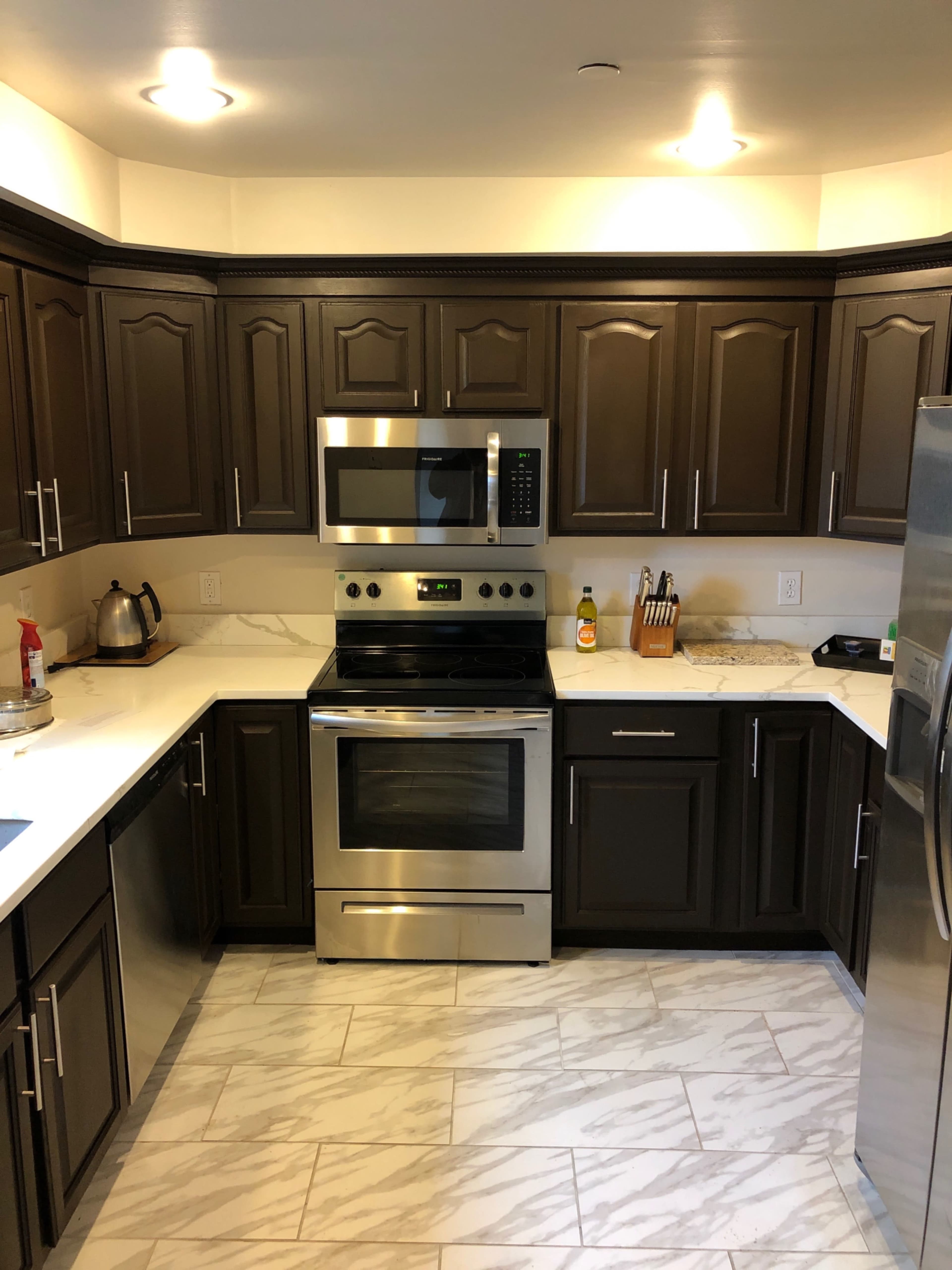 A modern kitchen with dark cabinetry, a stainless steel stove and microwave, and a marble countertop.
