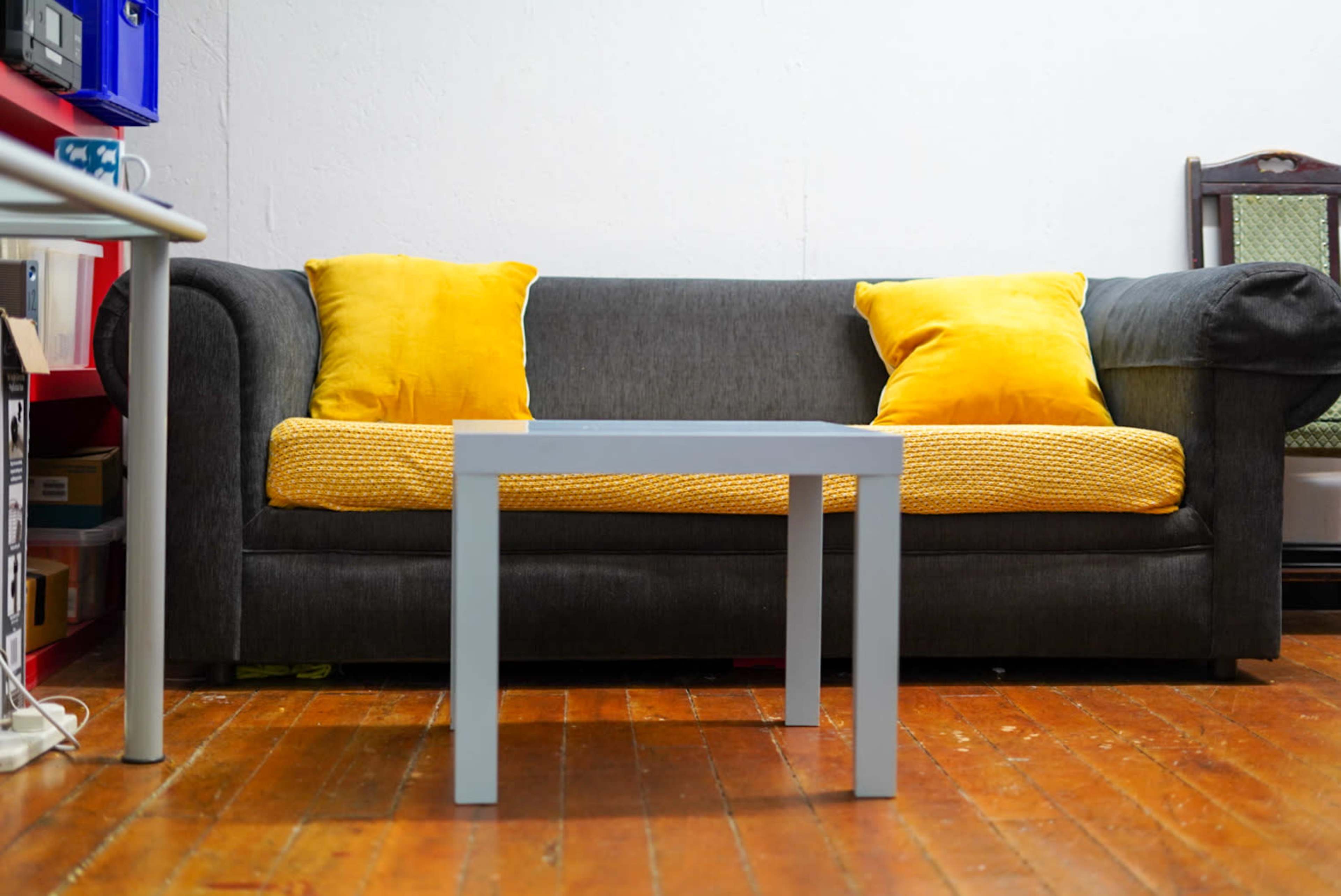 A gray couch with yellow cushions sits across from a small light-colored table on a wooden floor.