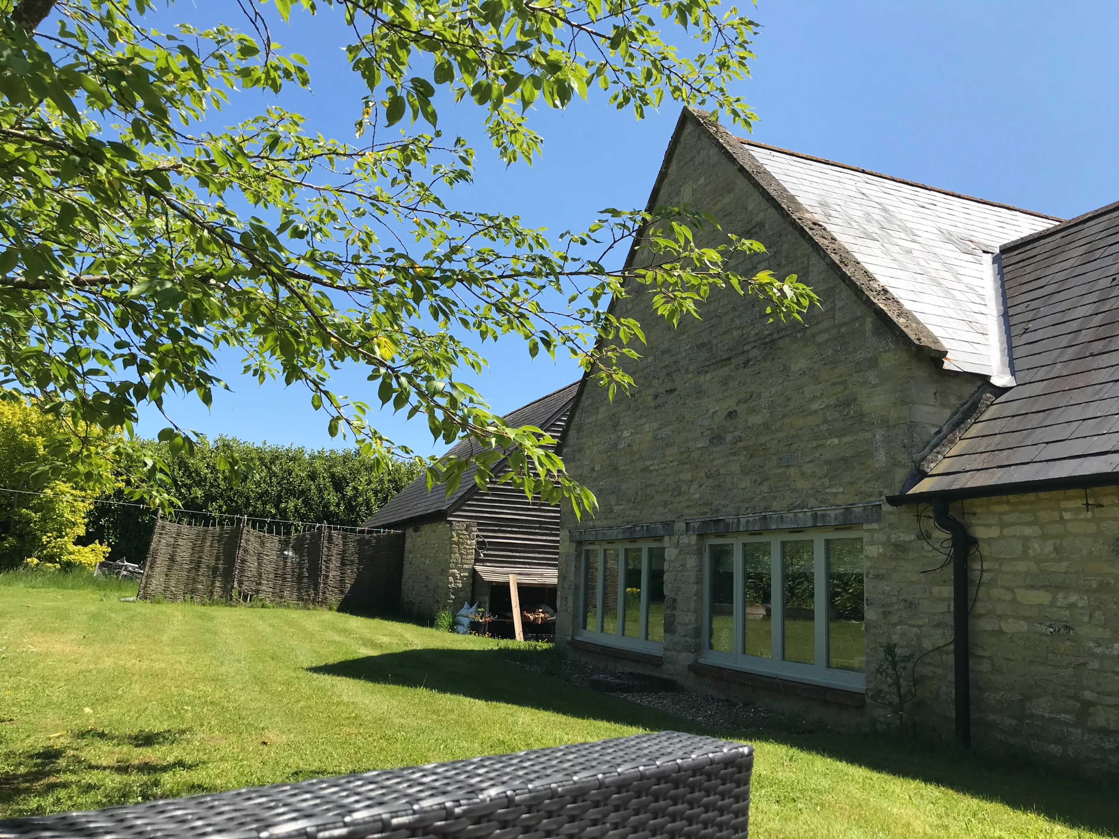 A stone house with a sloped roof sits in a green yard under a clear blue sky.