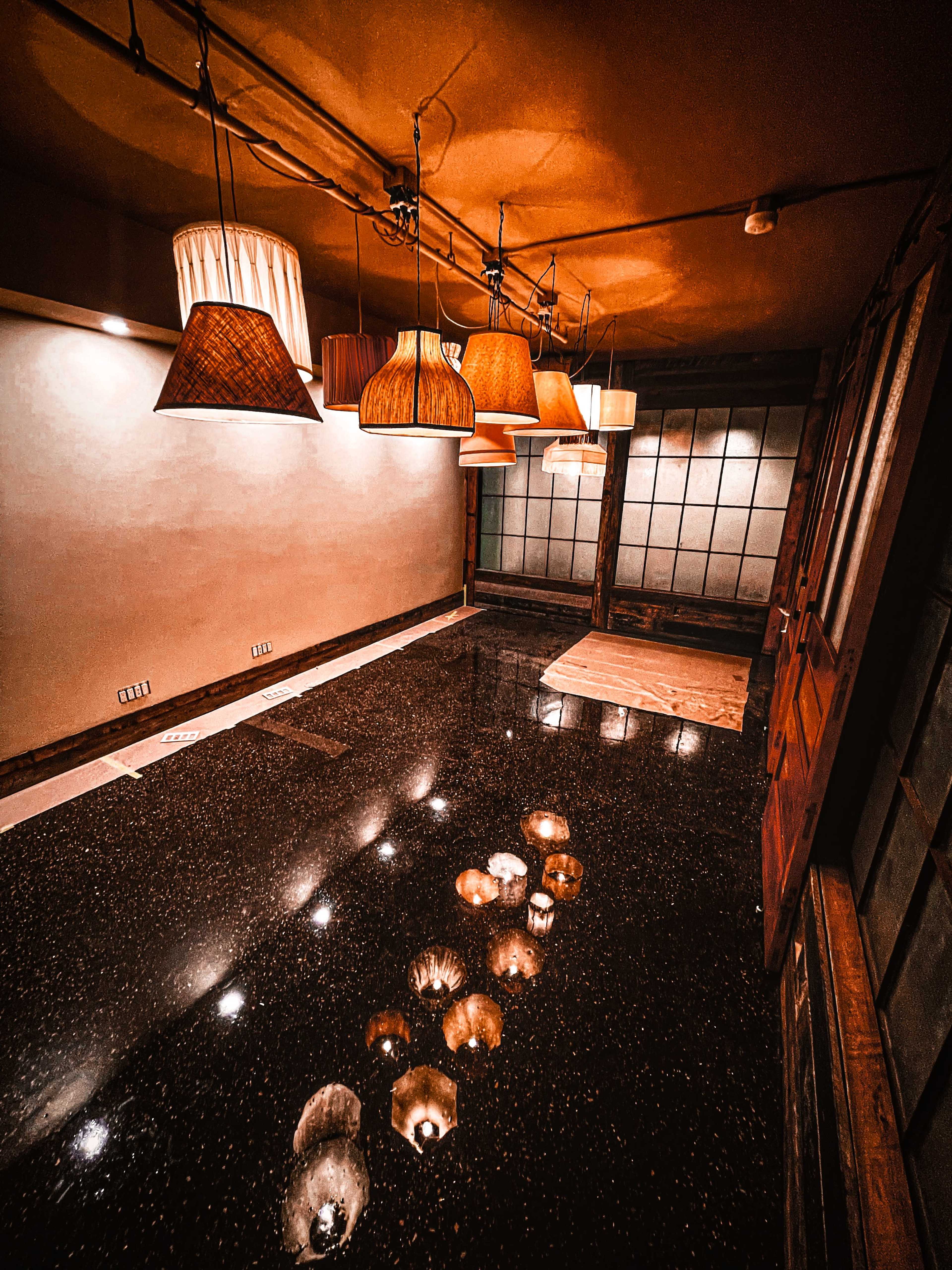 A dimly lit room featuring various hanging lamps, with a polished dark floor that reflects their light.