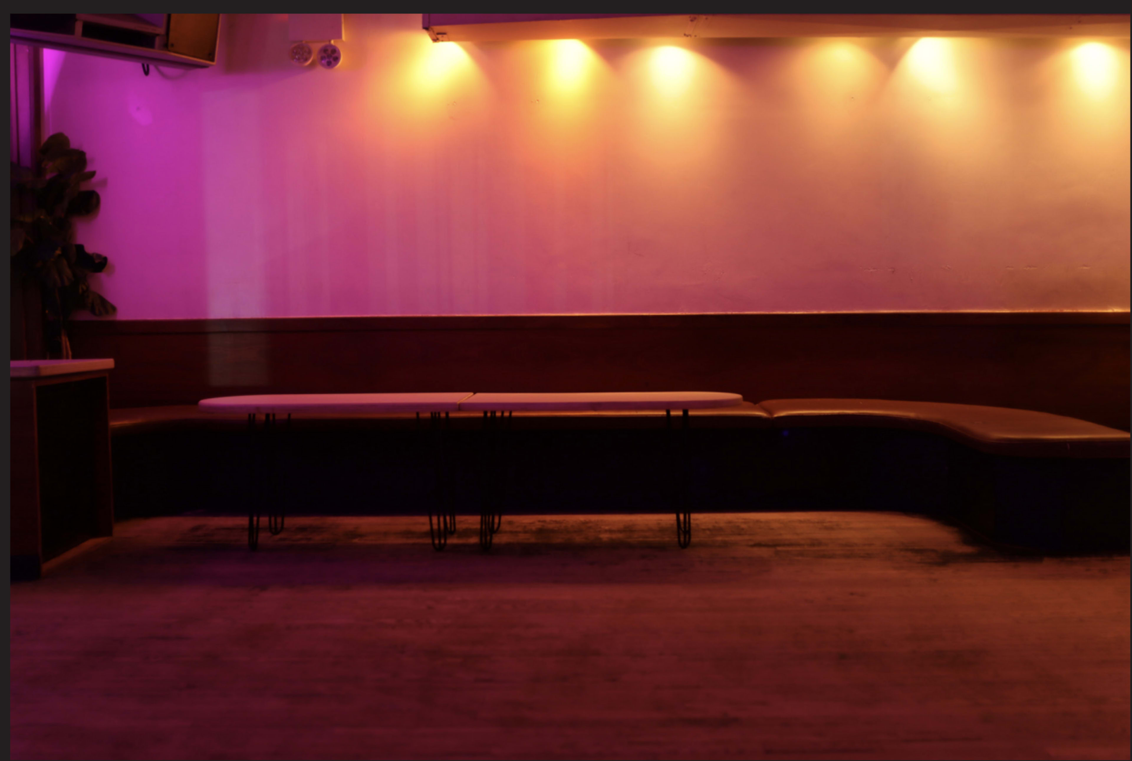 The image shows a dimly lit room with a long, curved bench along a wooden wall and subtle purple lighting above.