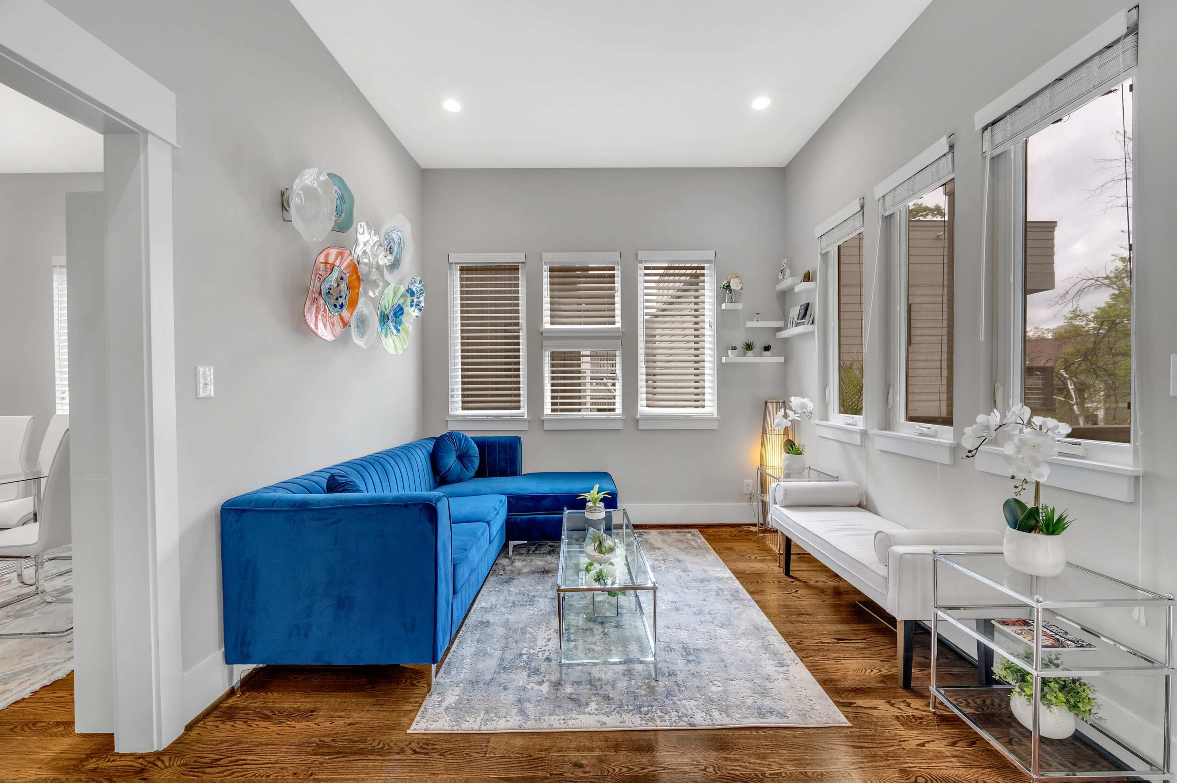 A well-lit living room featuring a blue sectional sofa, a glass coffee table, and decorative wall art.