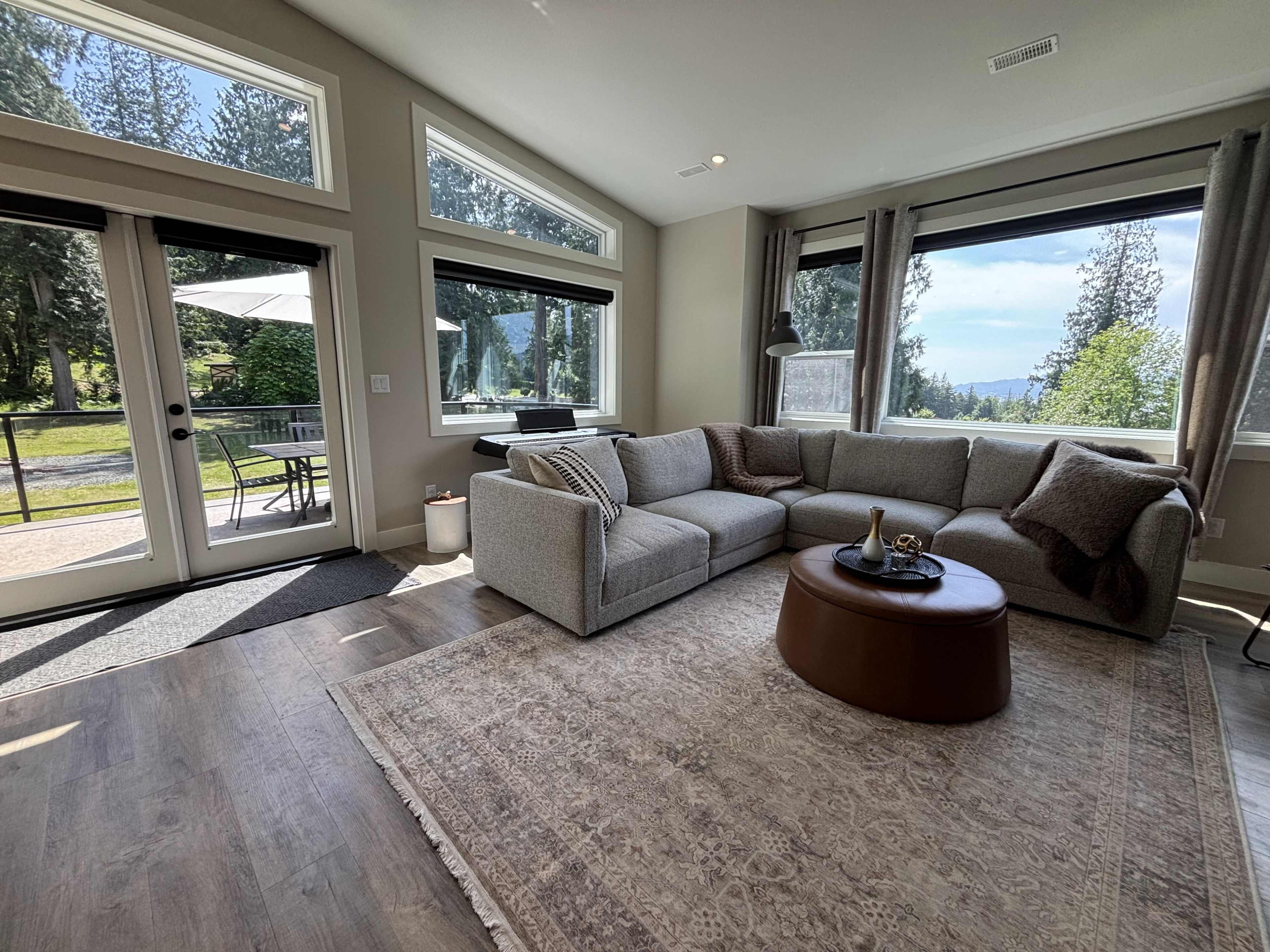 The image shows a modern living room with a large sectional sofa, a round coffee table, and large windows that provide a view of the outdoors.