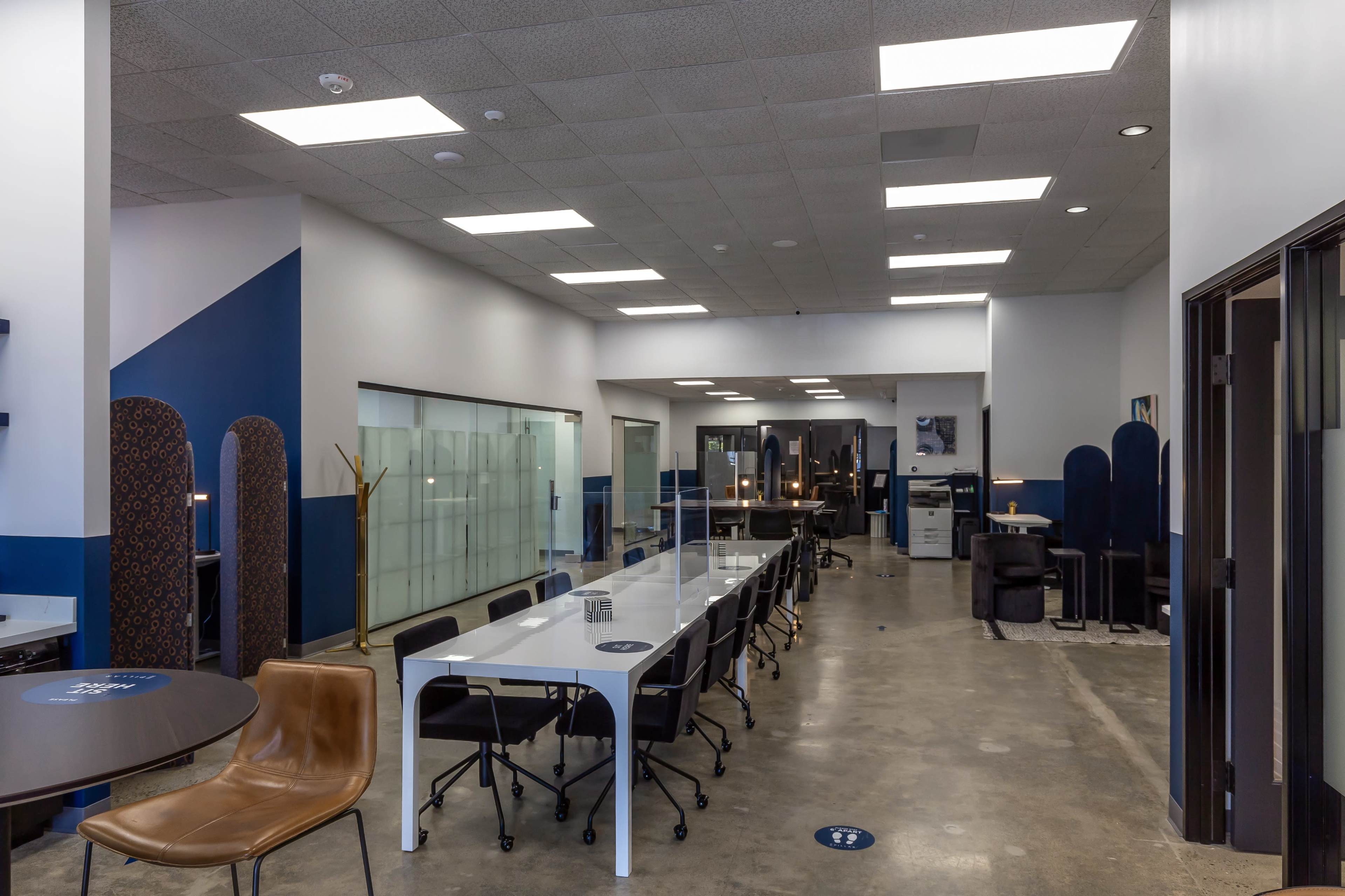 A modern office space with a long white table, dark chairs, and a glass wall separating different areas.