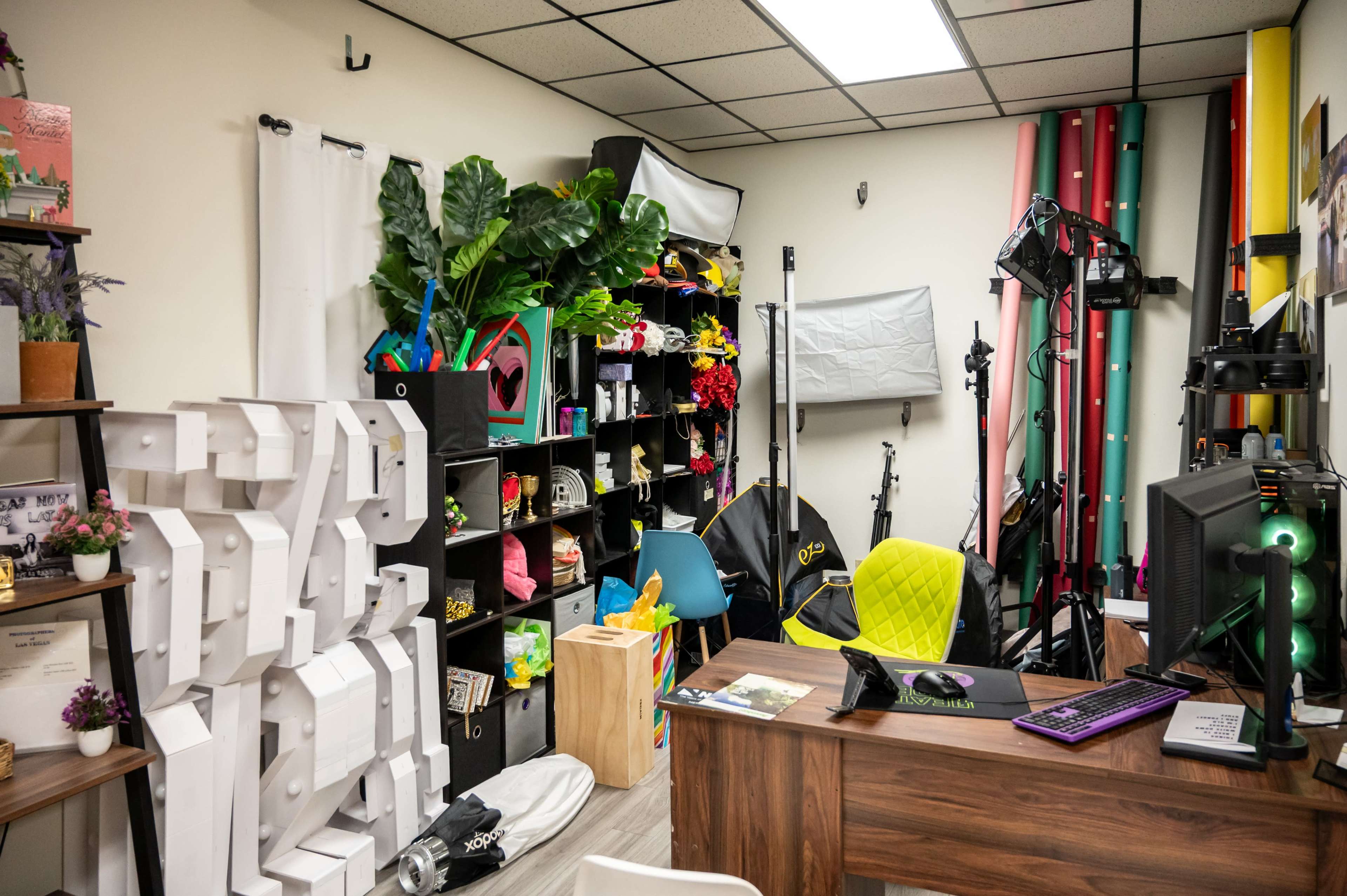 The image shows a cluttered photo studio with various backdrops, lighting equipment, and shelves filled with props and decorations.