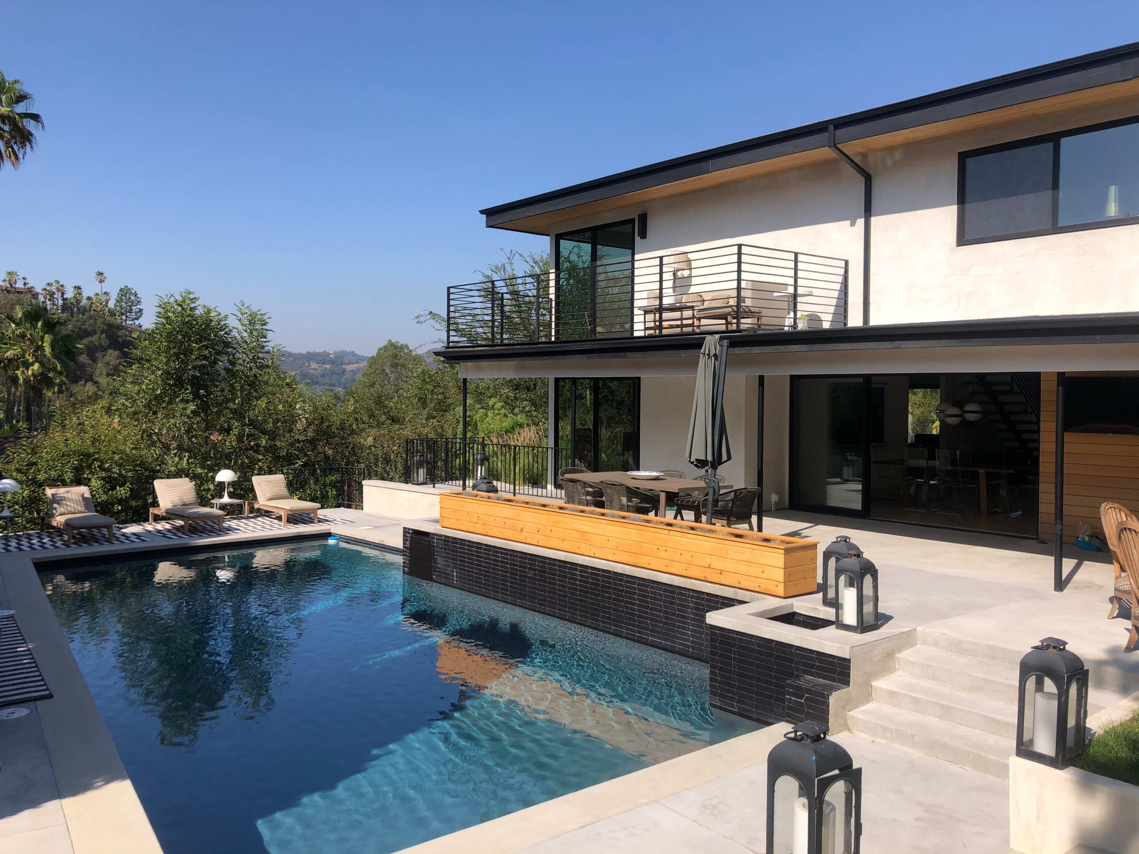 A modern house with a swimming pool and a wooden deck surrounded by lush greenery.