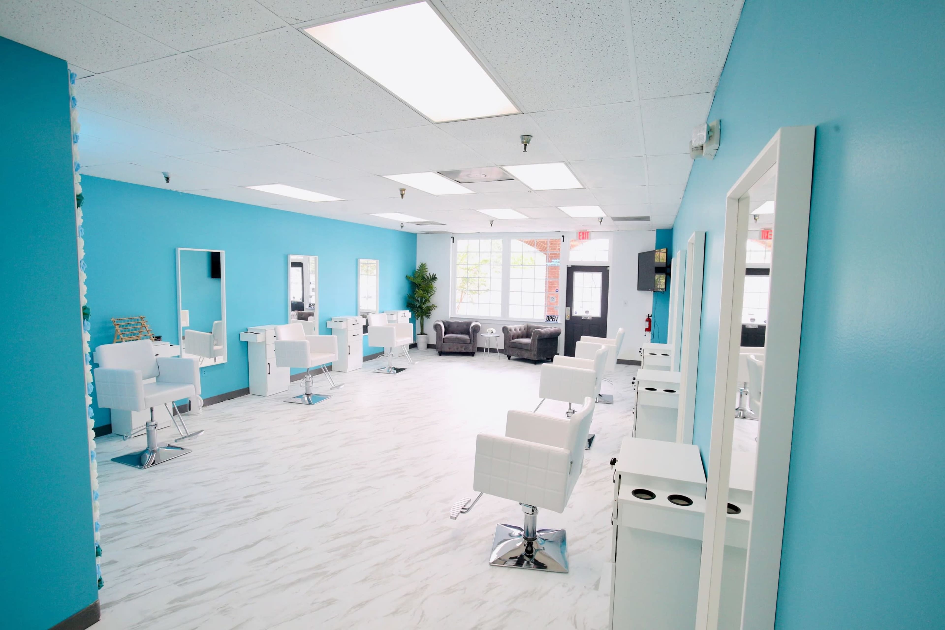 A brightly colored salon interior with white styling chairs, wooden accents, and large windows.