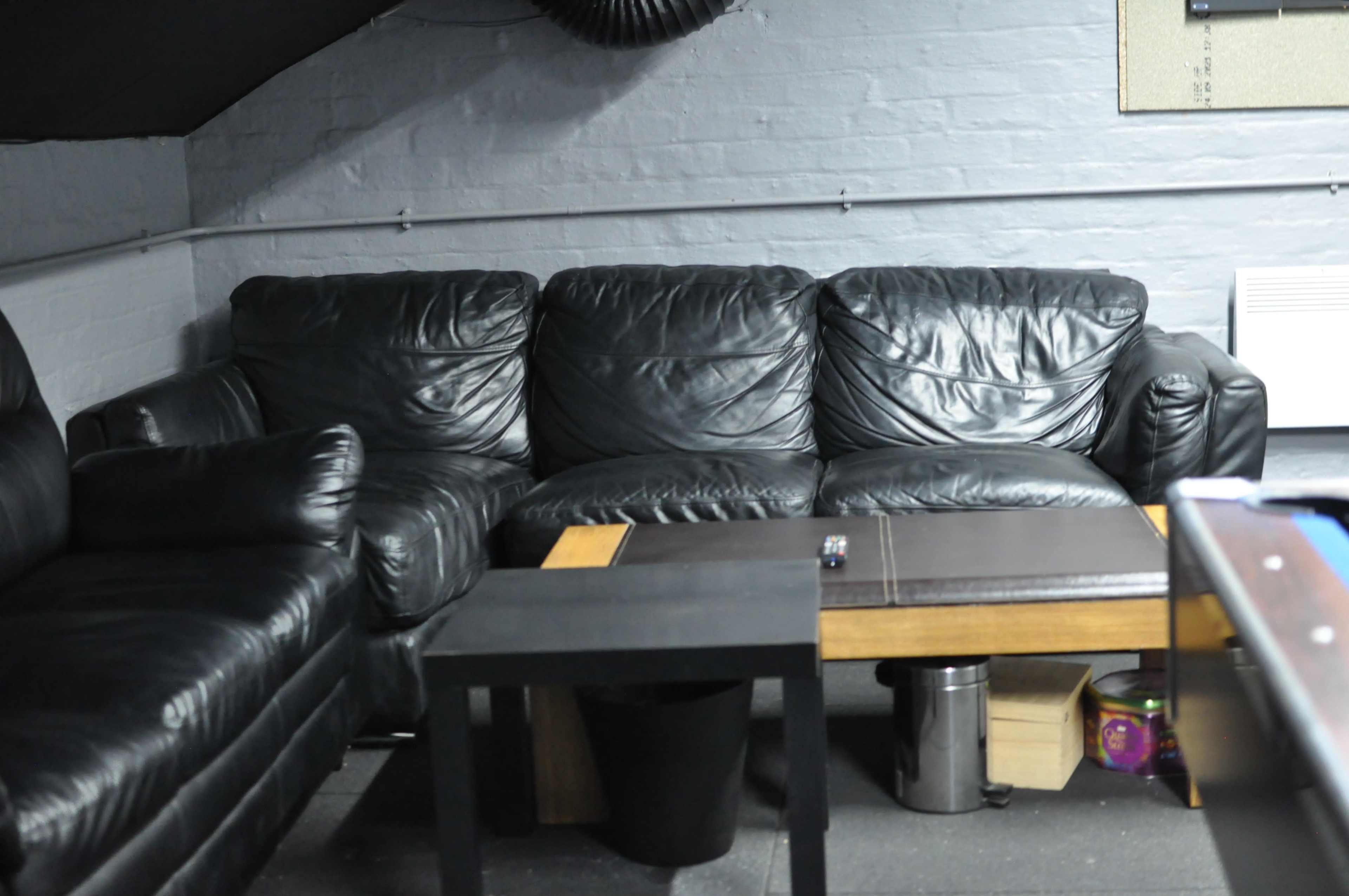 The image shows a black leather couch beside a small wooden coffee table in a dimly lit room.