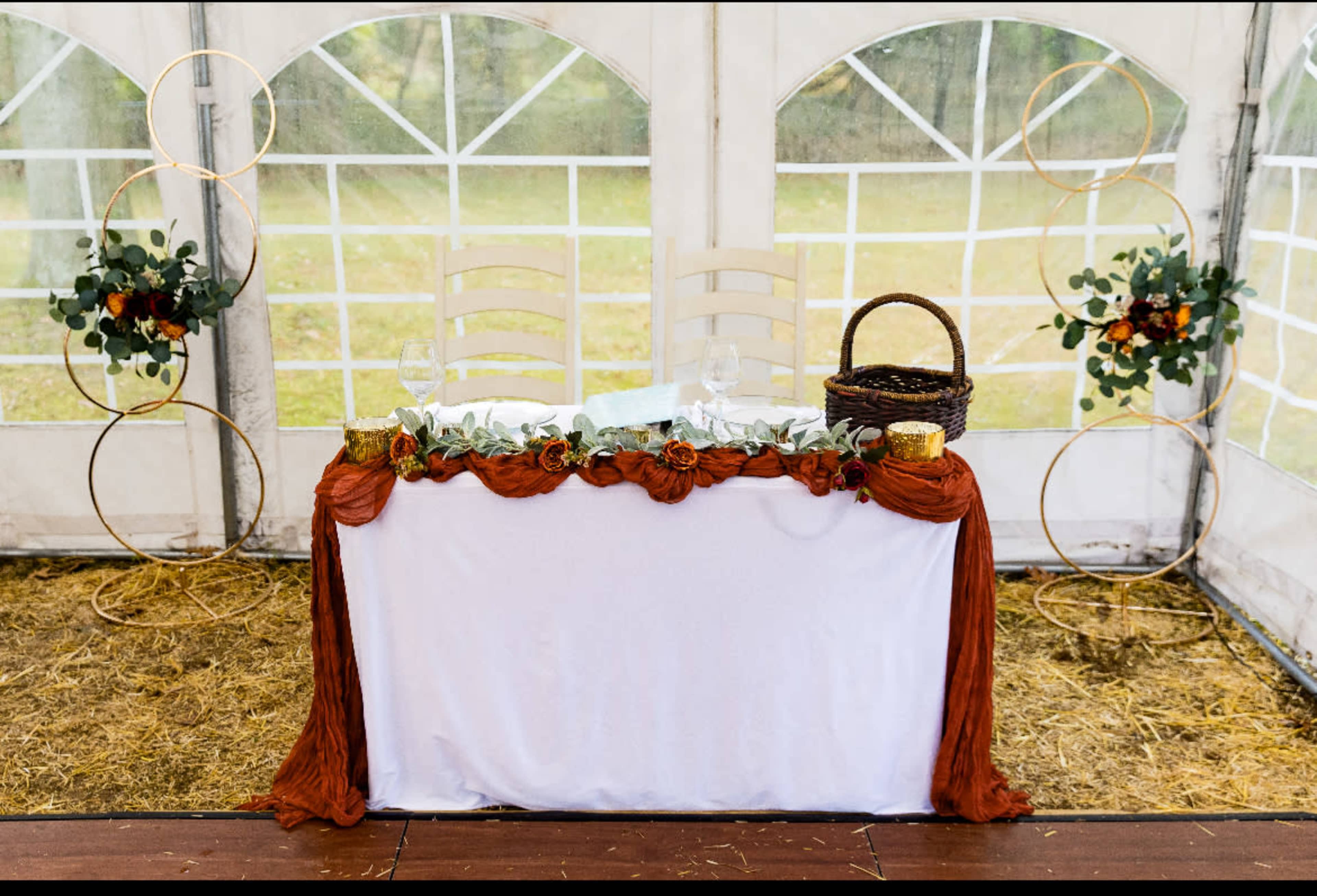 A decorated table for a special event is set inside a tent, featuring floral arrangements, a basket, and elegant tableware.