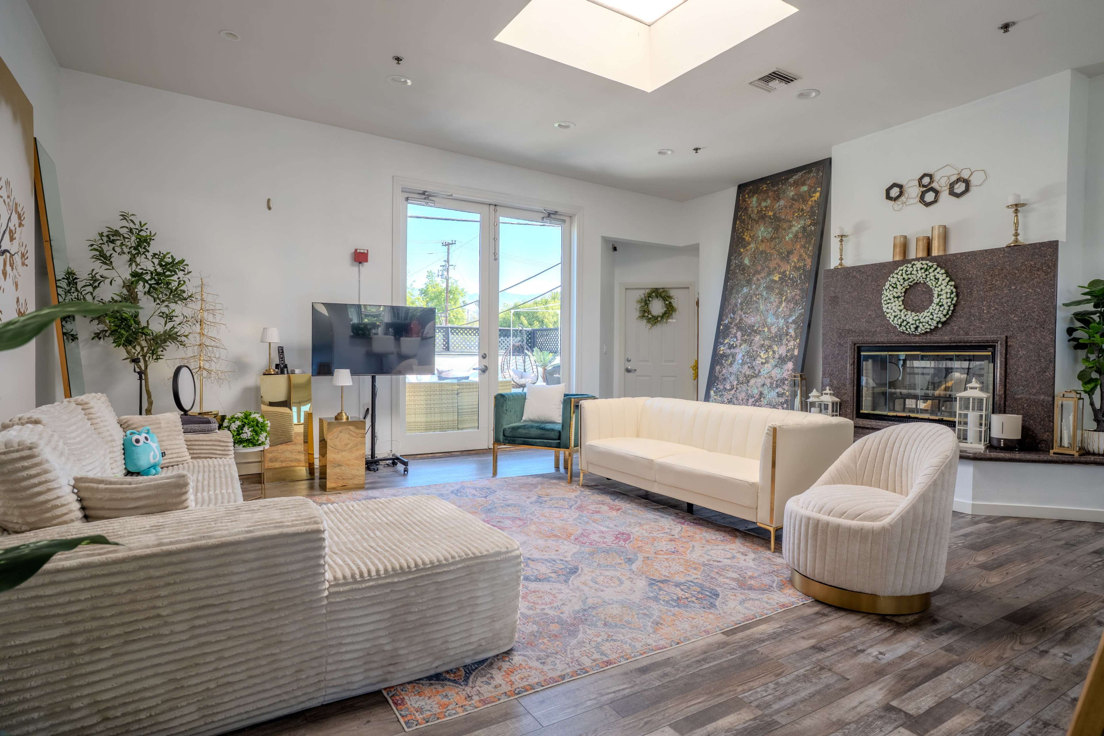 The image shows a bright living room with a seating arrangement that includes a cream-colored sofa, two armchairs, and a rug, along with a large window and a fireplace in the background.