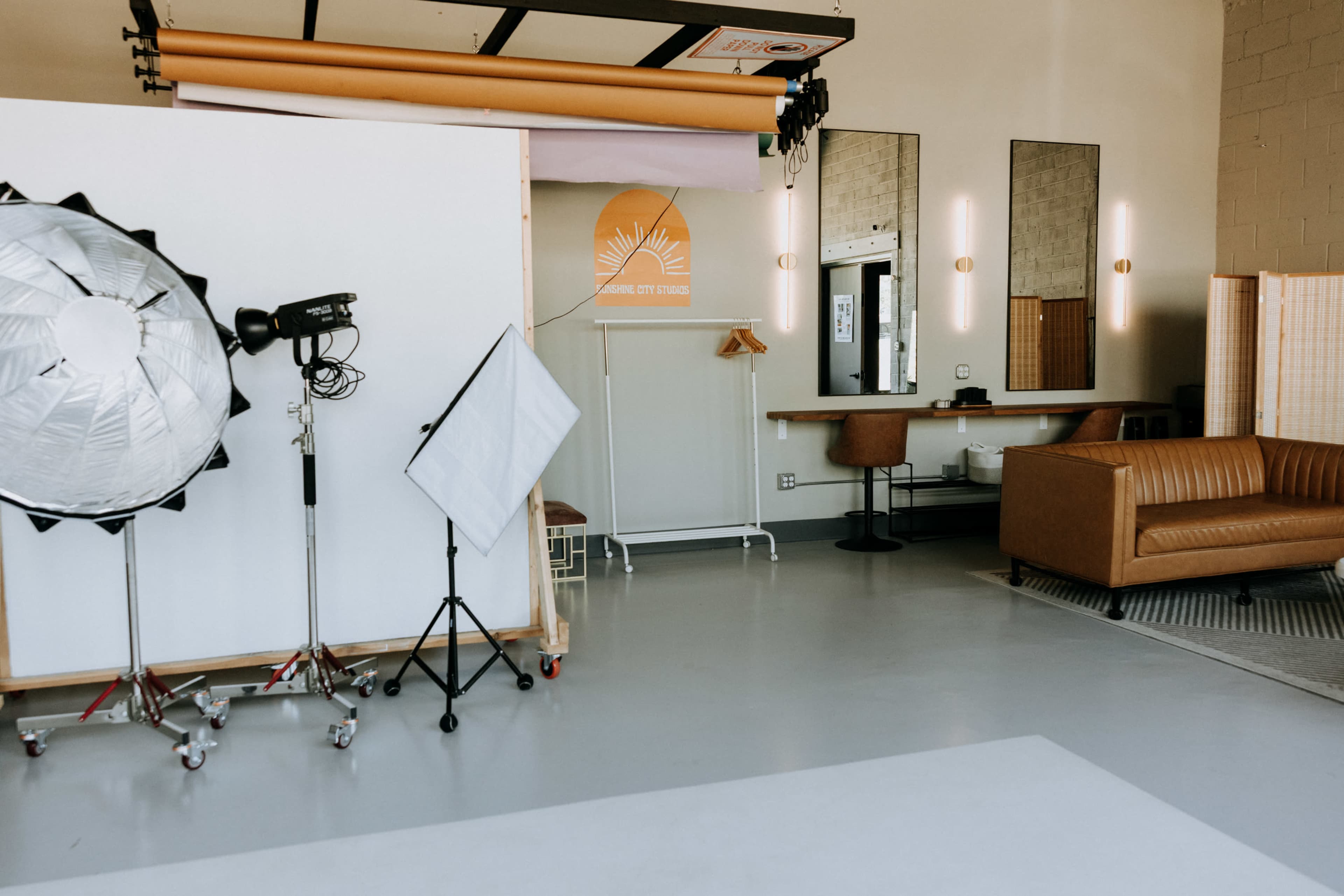 The image depicts a photography studio featuring a backdrop, lighting equipment, mirrors, and a brown leather sofa.