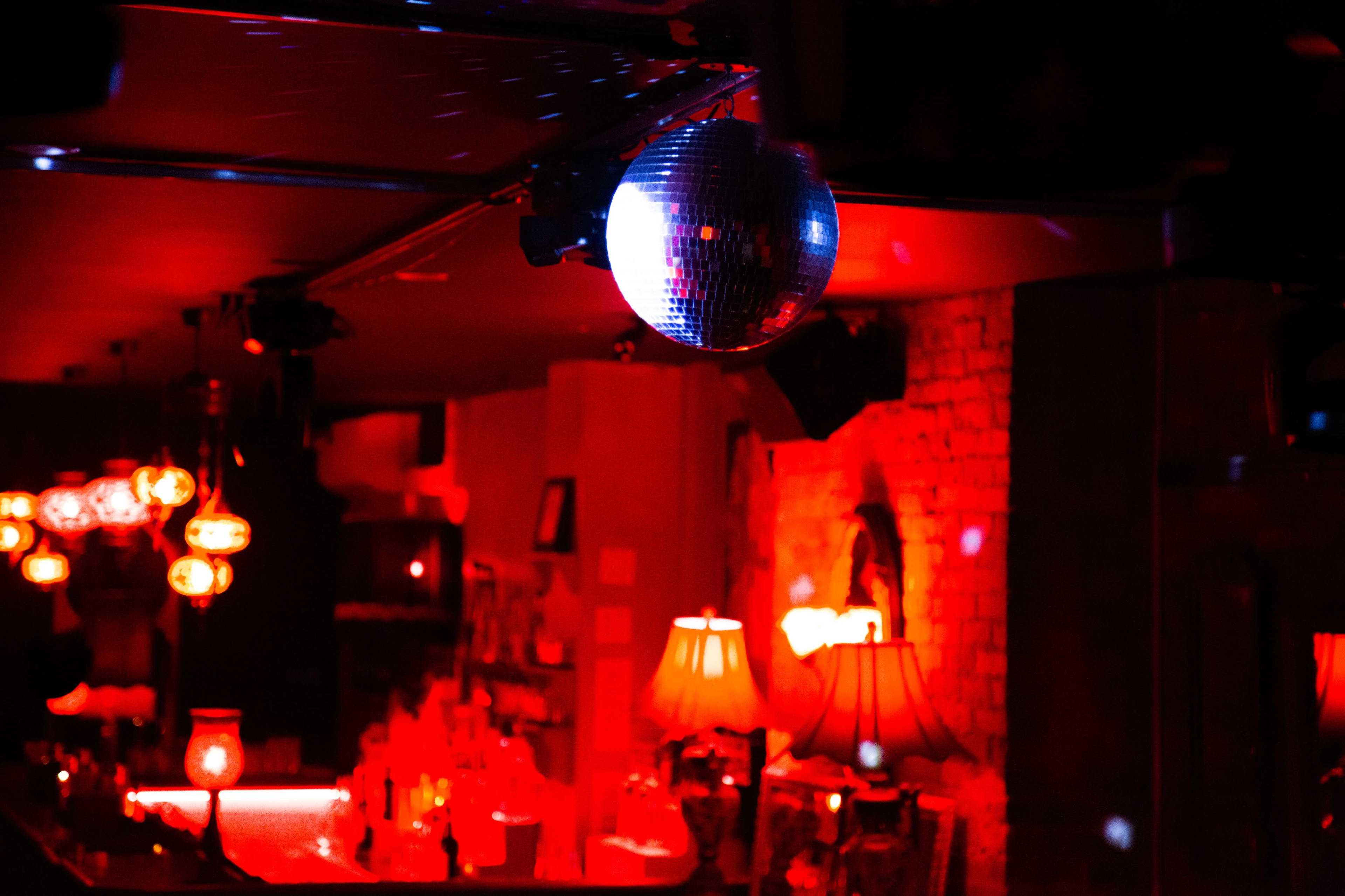 A disco ball hangs above a bar illuminated by red and soft amber lighting.