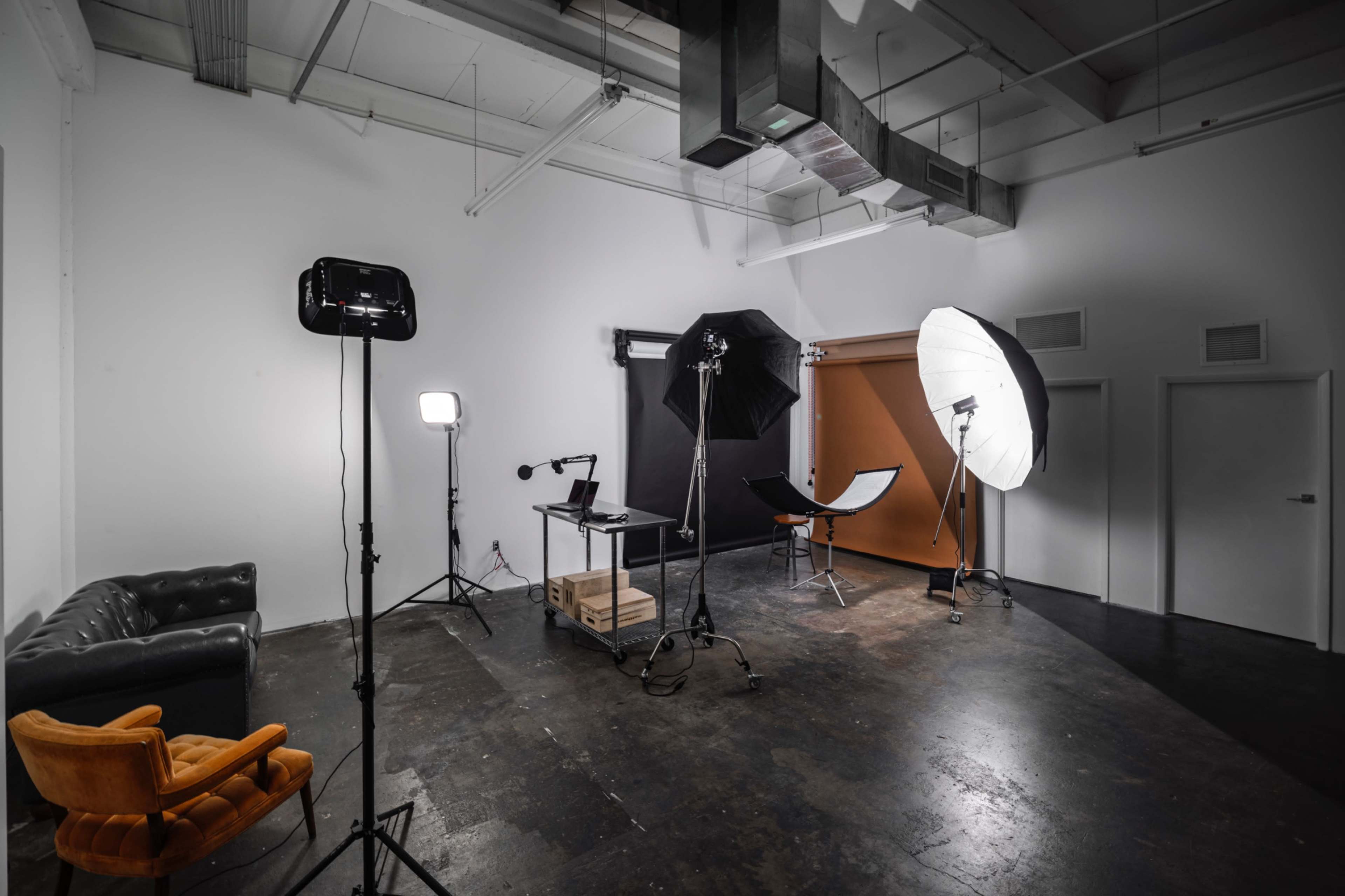 The image shows a photography studio with various lighting equipment, a backdrop, and a seating area.