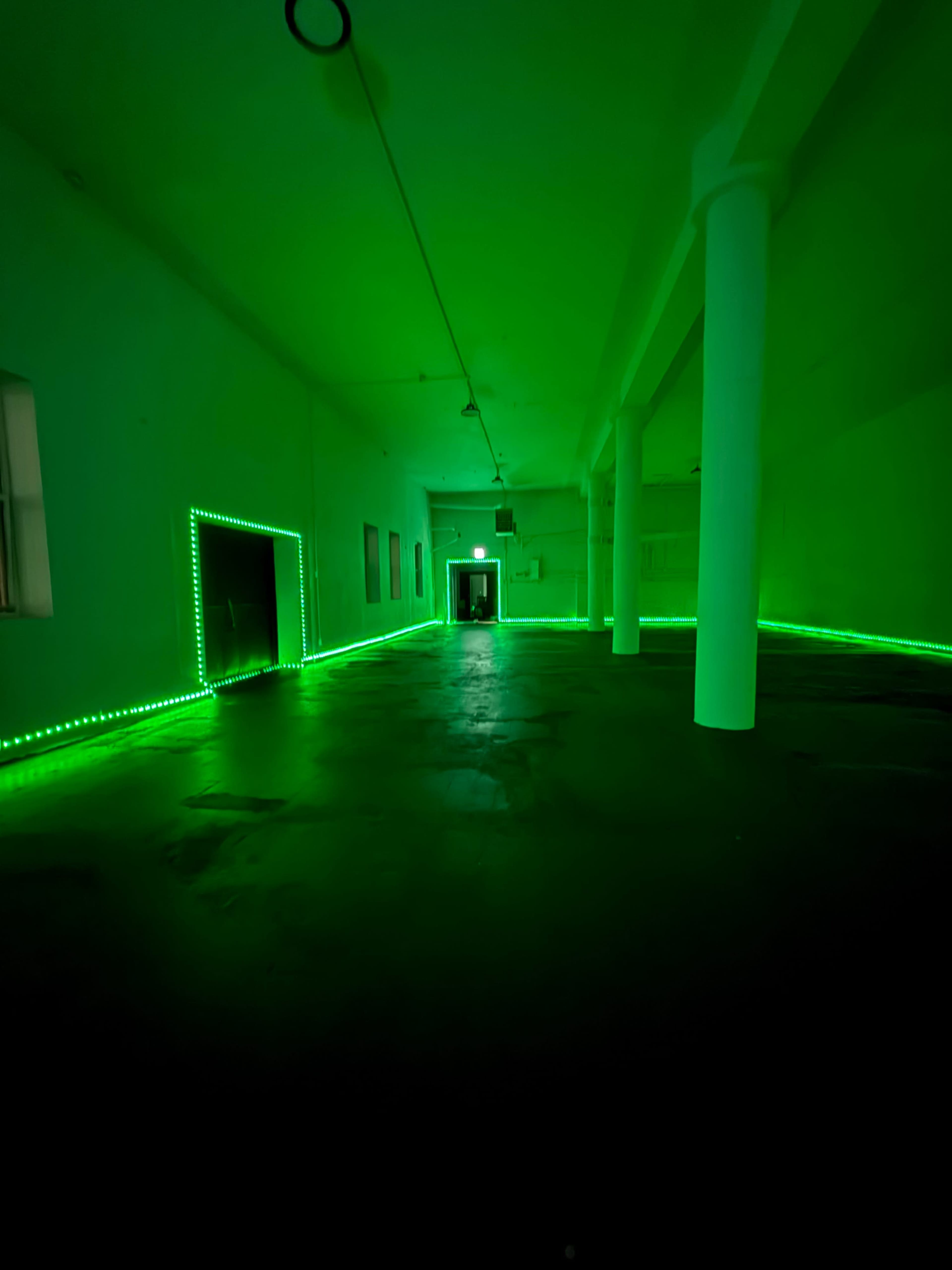 The image shows a spacious, dimly lit room with green LED lights outlining doorways and the perimeter of the floor.
