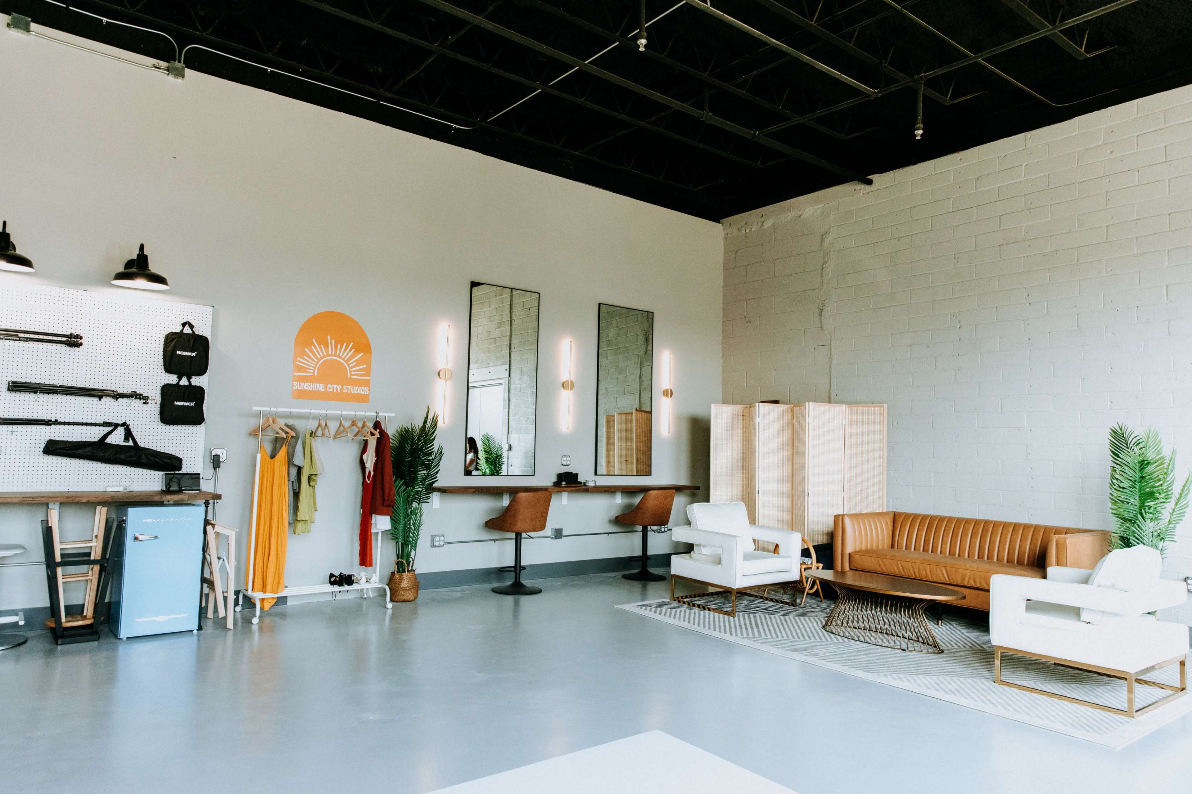 A modern, spacious salon with a seating area, styling stations, and clothing racks against a light-colored wall.