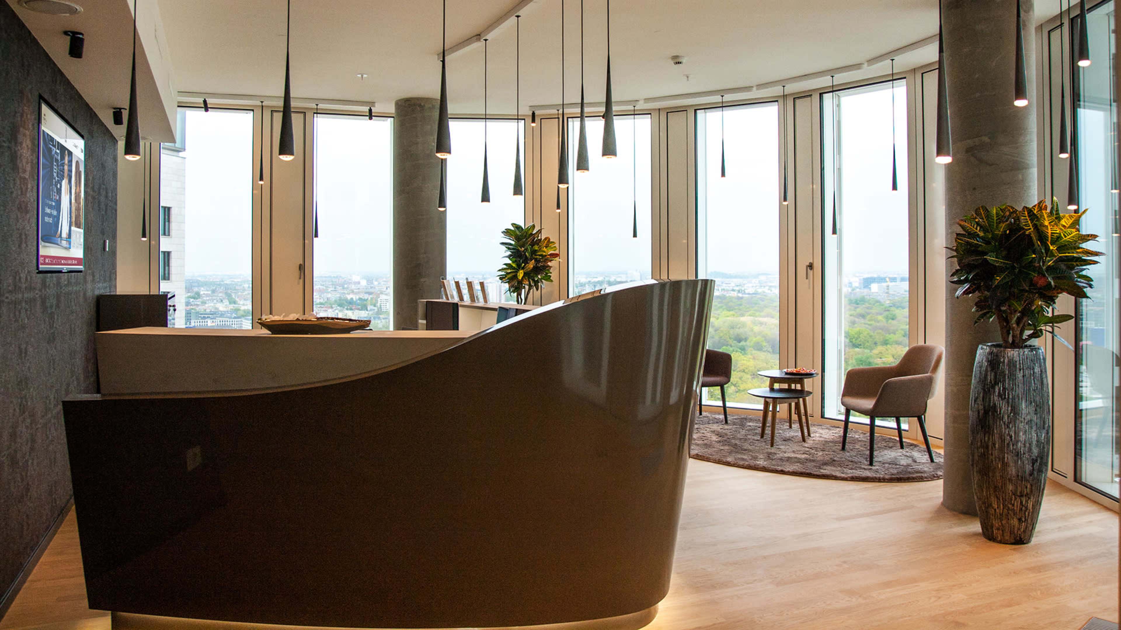 A modern reception area with a curved desk, two chairs, and large windows providing a view of the cityscape.