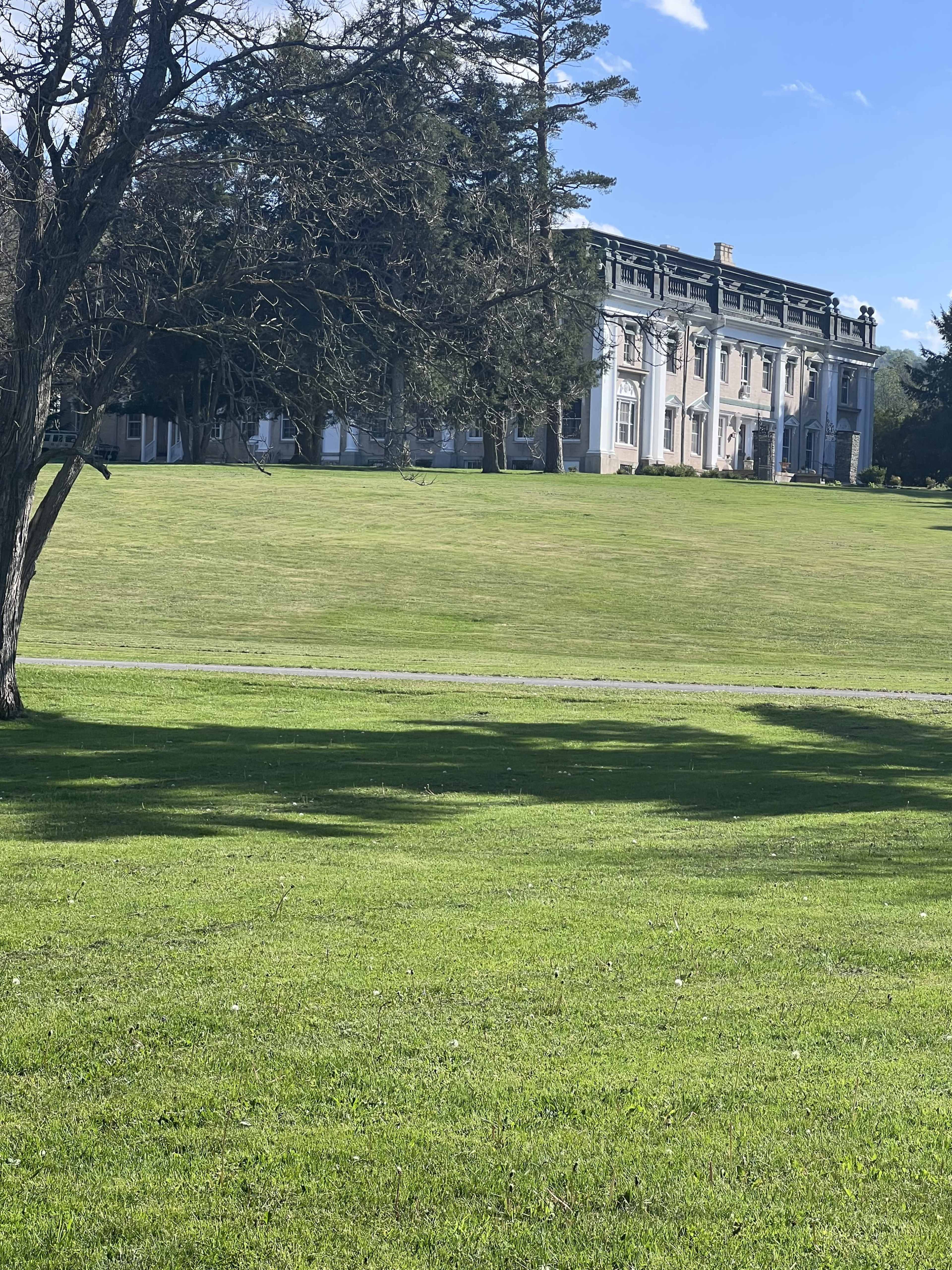 A large, stately building is visible in the background, framed by a well-maintained green lawn and a few trees.