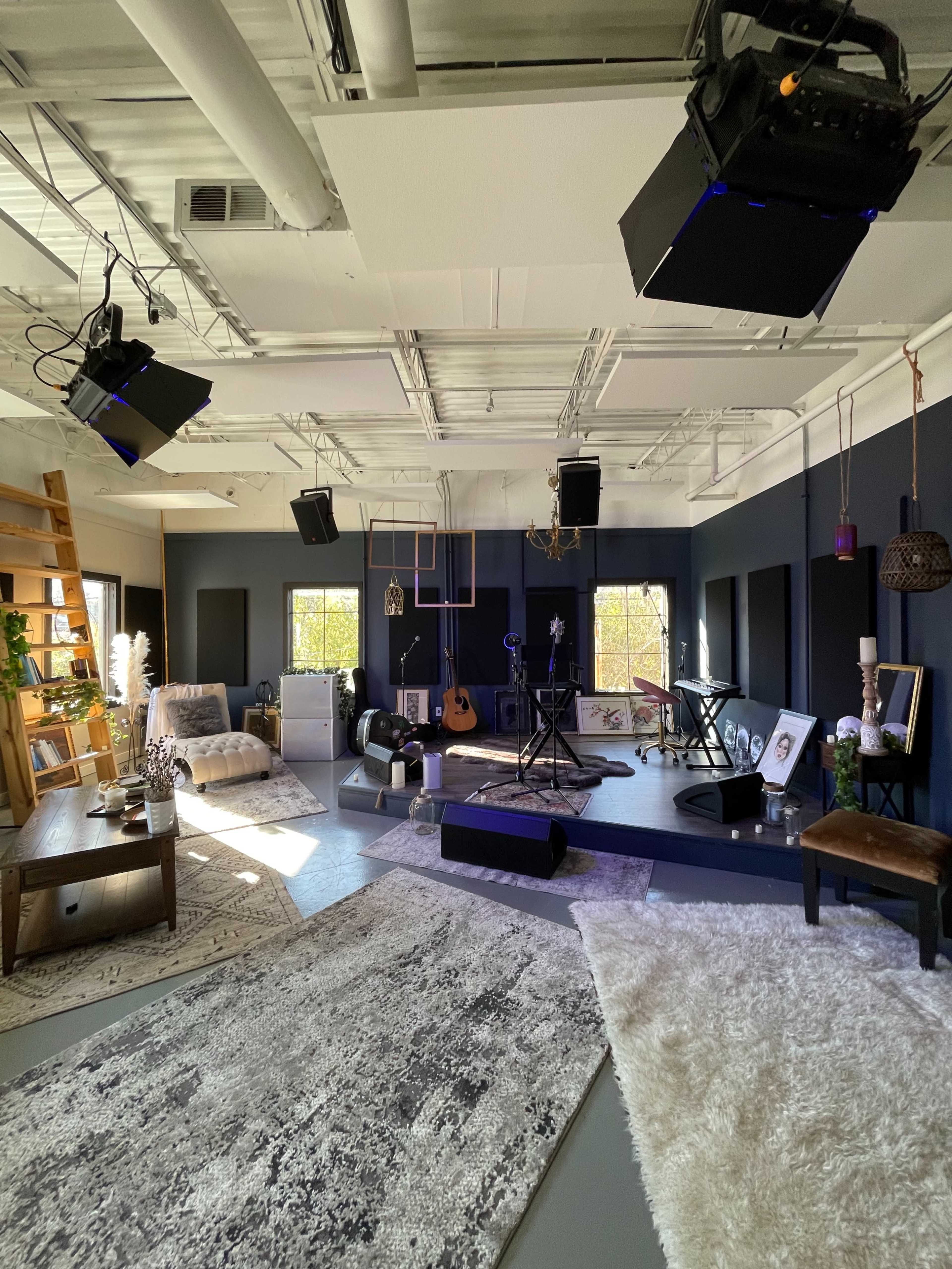 The image shows a well-lit recording studio featuring a variety of musical instruments, decorative furniture, and a carpeted floor.