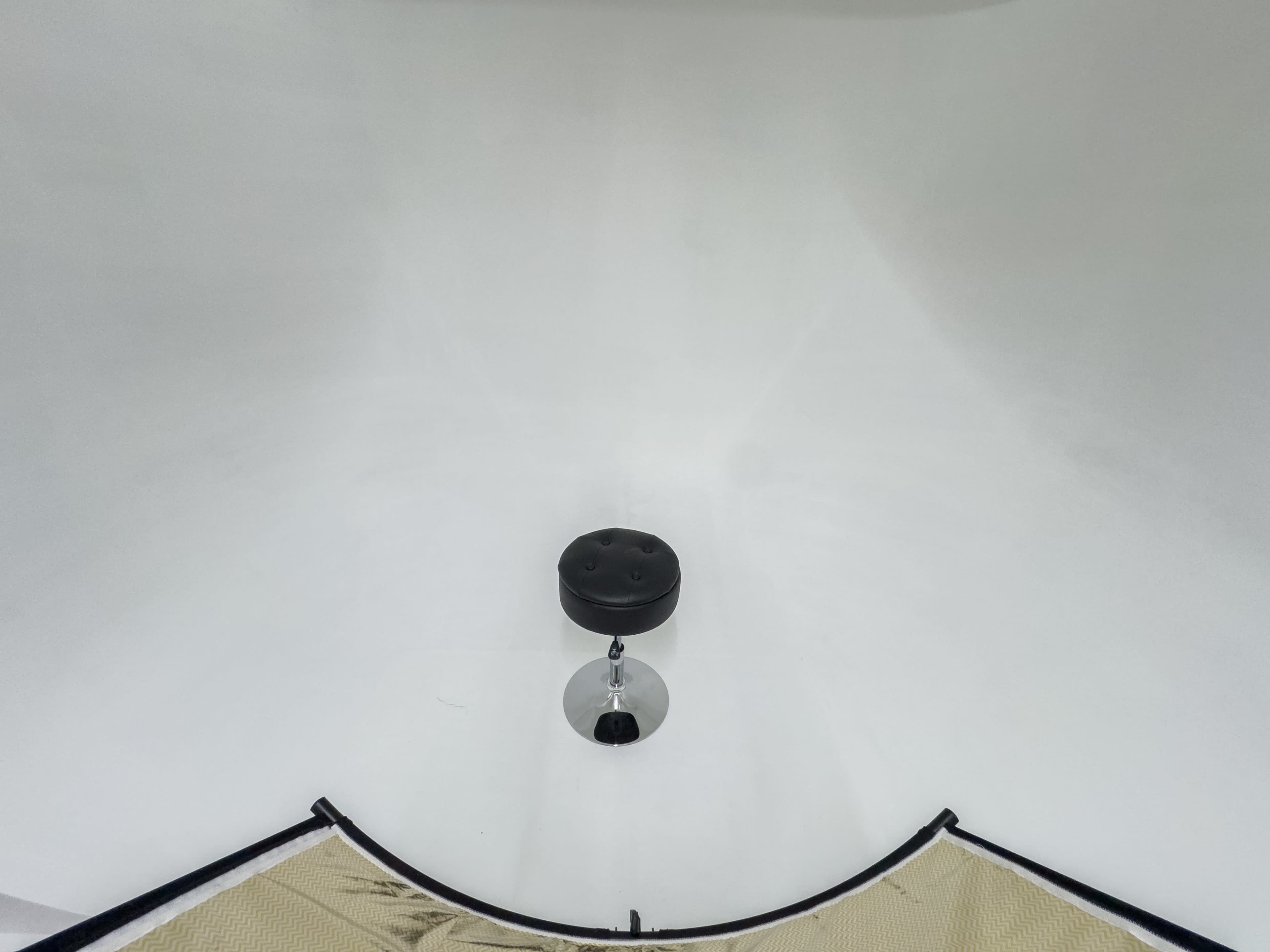 A black stool is placed on a white background, surrounded by a beige mat.