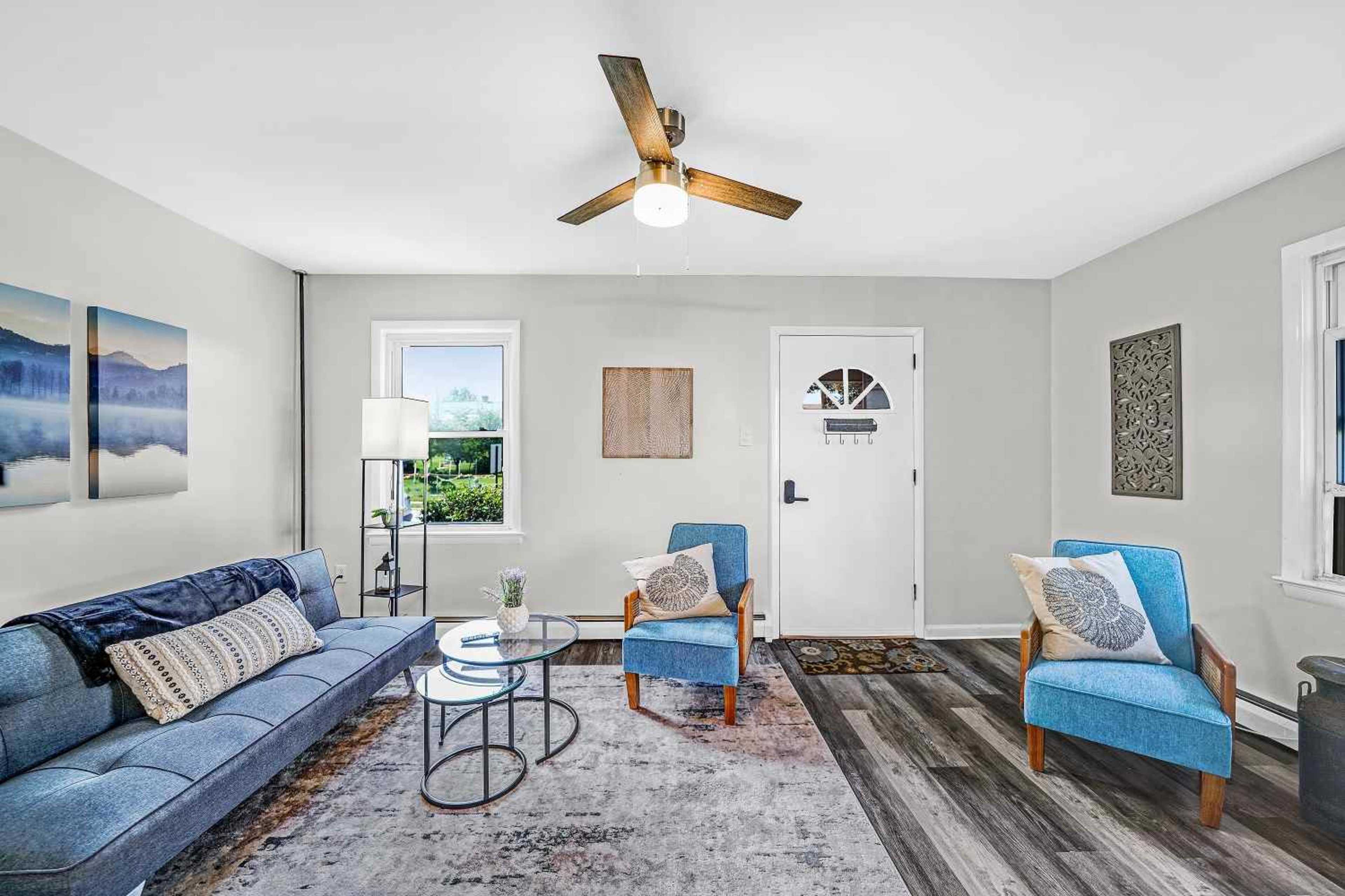 A living room featuring a blue sofa, two blue armchairs, a round glass coffee table, and a door with a window, all set against a light green wall.